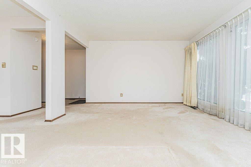 Living area featuring light-colored carpeting, white walls, and a large window with sheer and opaque curtains - 8804 19 Avenue, Edmonton, AB - Indoor Photo Showing Other Room