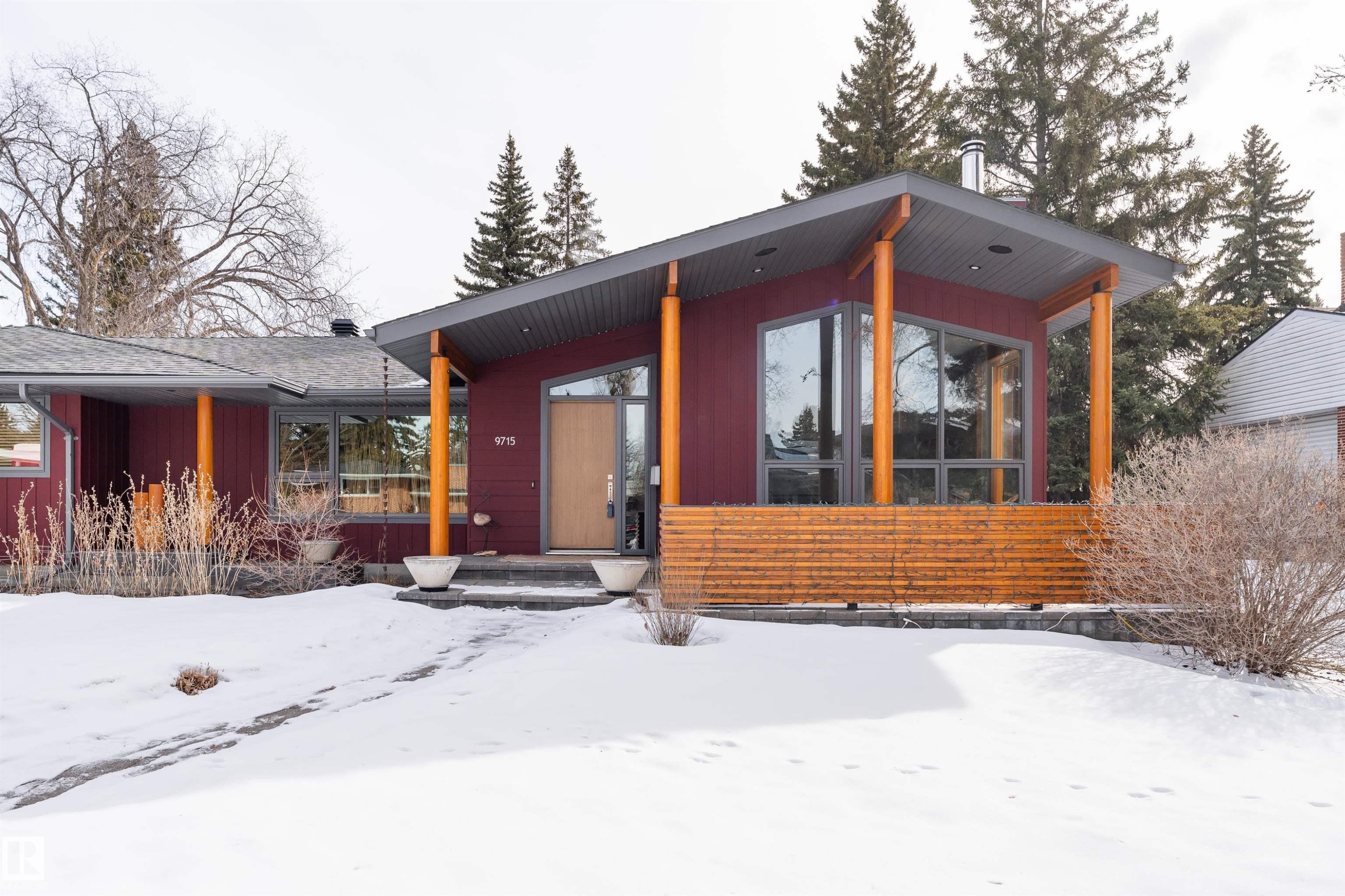 The property features a contemporary architectural style with a prominent sloped roofline, large windows, and natural wood accents - 9715 141 Street Nw, Edmonton, AB - Outdoor With Deck Patio Veranda