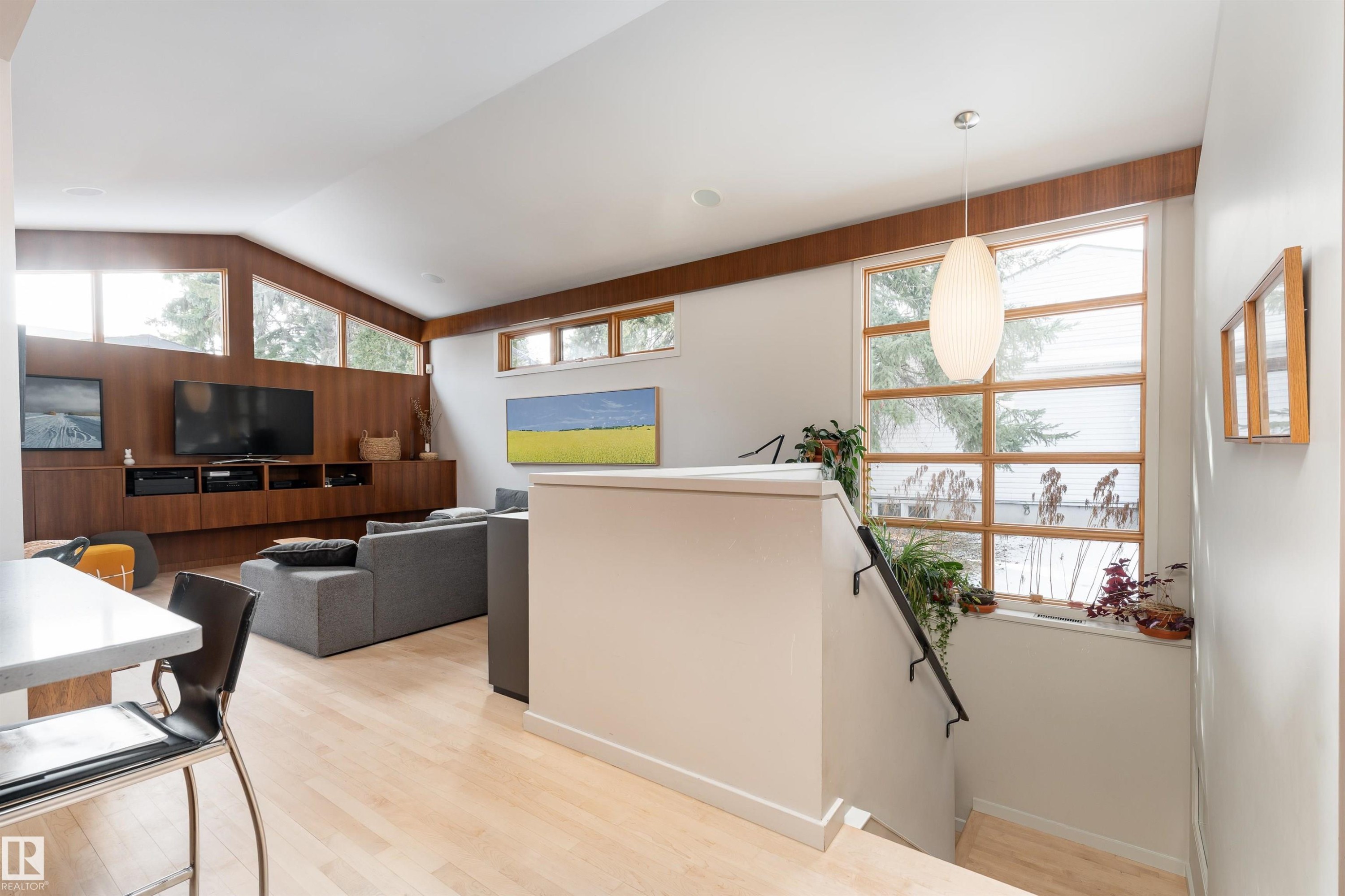 The property features a bright living area with light hardwood floors, a built-in media console, and large windows - 9715 141 Street Nw, Edmonton, AB - Indoor Photo Showing Other Room