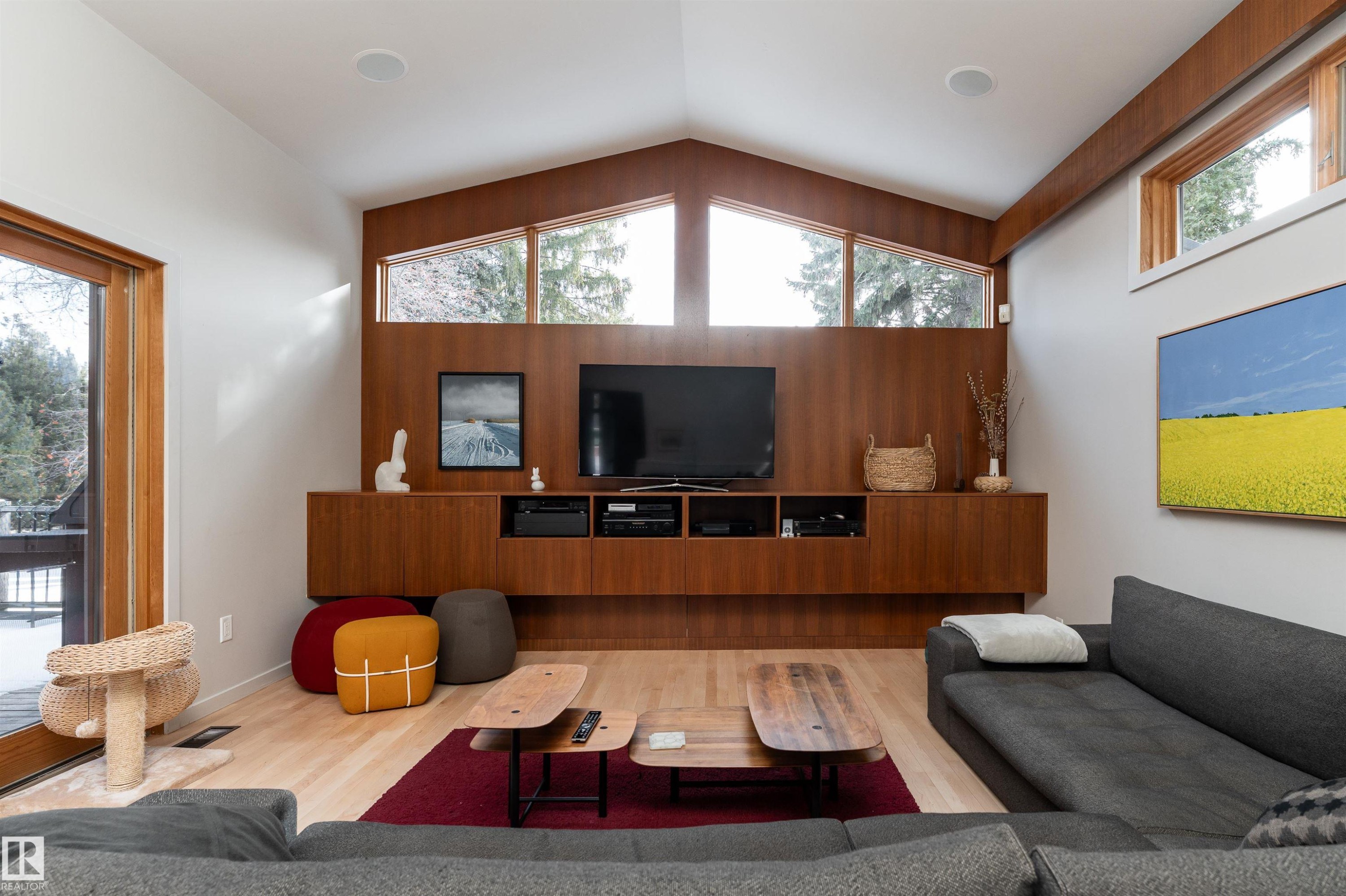 Living area featuring light wood flooring, a built-in media console with wood paneling, and an expansive window with a view of trees - 9715 141 Street Nw, Edmonton, AB - Indoor Photo Showing Living Room
