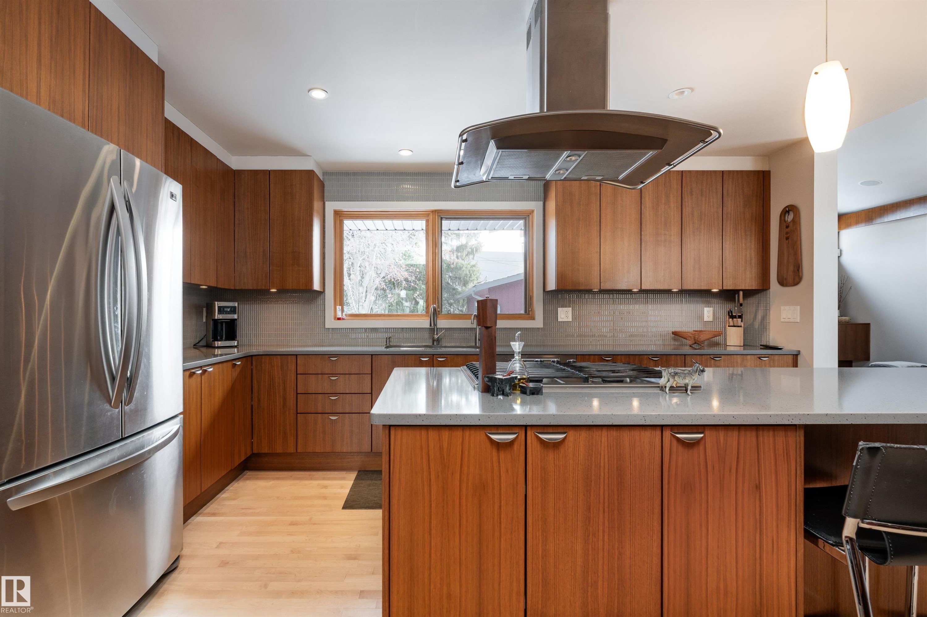 The kitchen features stainless steel appliances, wood cabinetry, light-colored countertops, and a tiled backsplash - 9715 141 Street Nw, Edmonton, AB - Indoor Photo Showing Kitchen