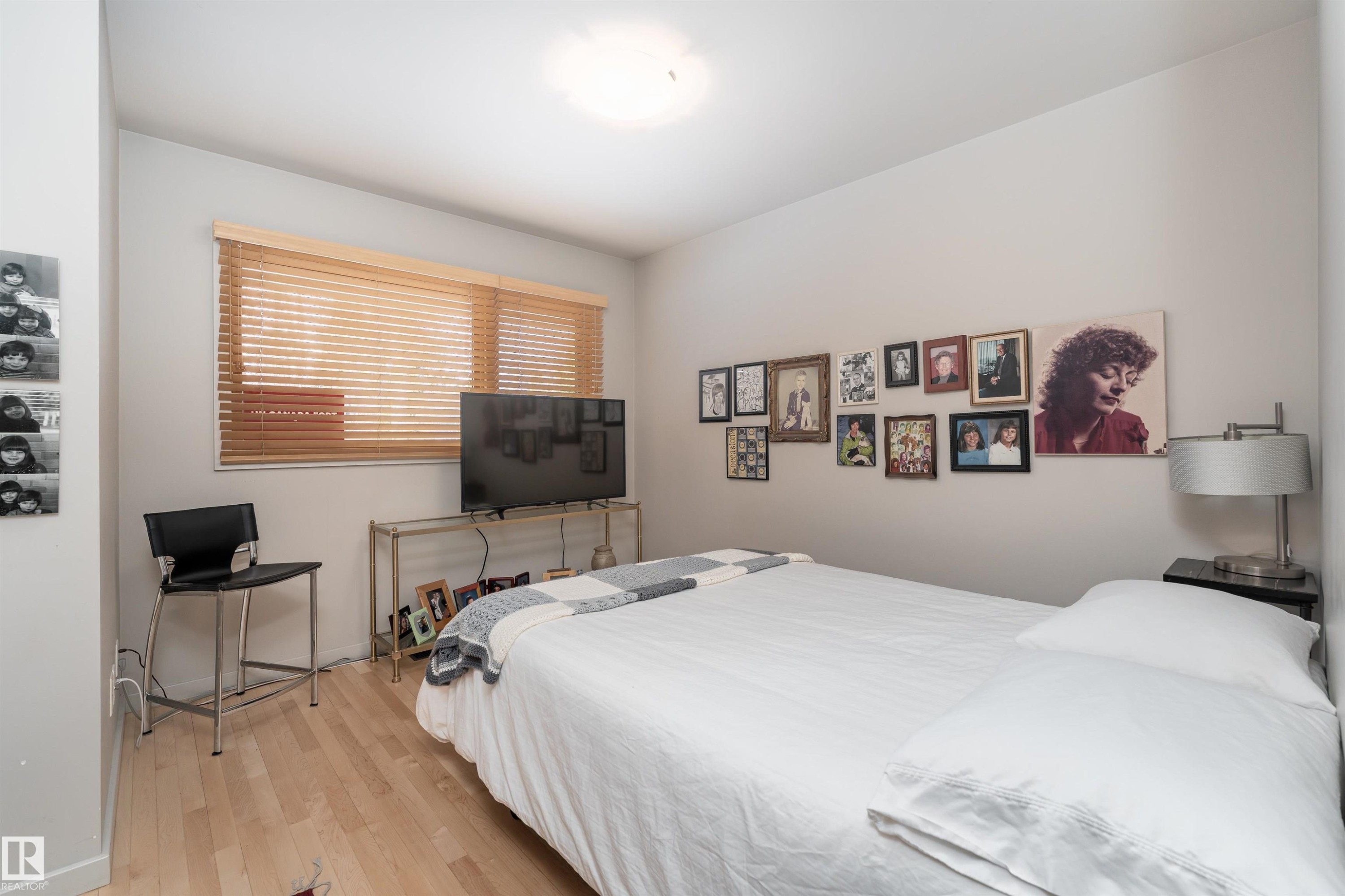 This room features light-toned hardwood flooring and a window with wooden blinds, offering natural light - 9715 141 Street Nw, Edmonton, AB - Indoor Photo Showing Bedroom