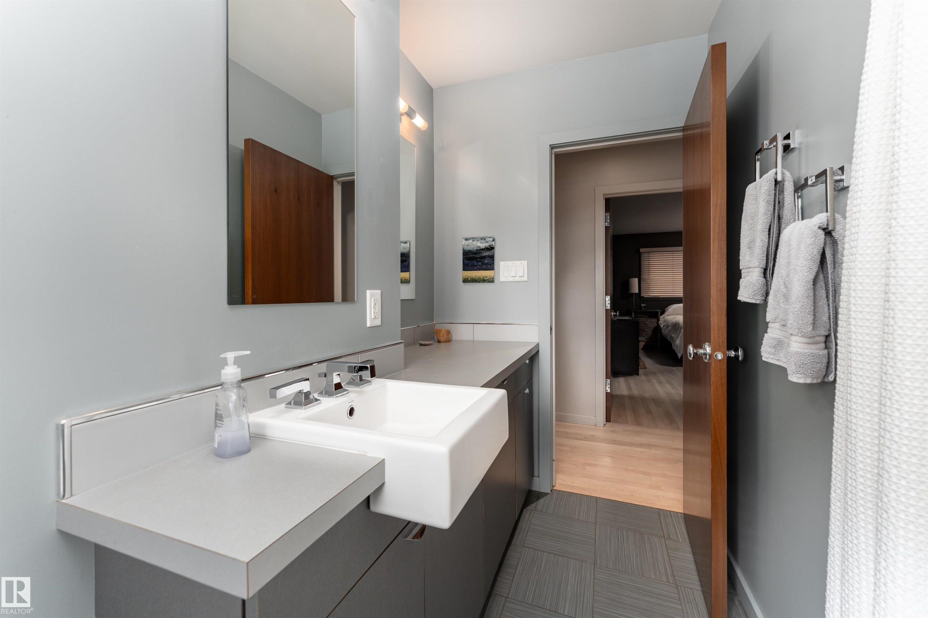 The bathroom features a vanity with a white rectangular sink, a large mirror, and light gray walls - 9715 141 Street Nw, Edmonton, AB - Indoor