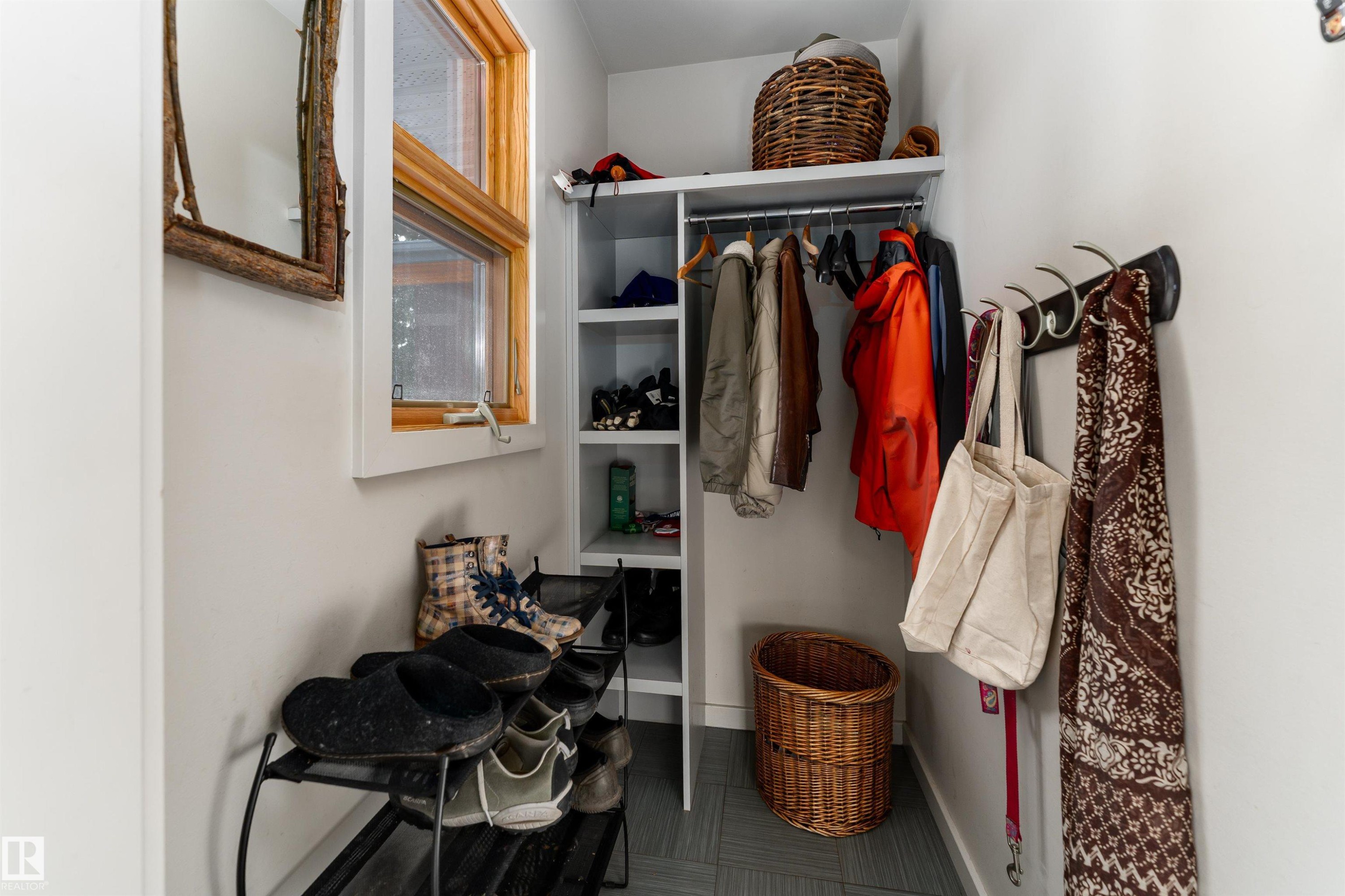 This area features a window with natural wood trim, a built-in storage system with shelving and hanging space, and a wall-mounted rack with hooks - 9715 141 Street Nw, Edmonton, AB - Indoor Photo Showing Other Room