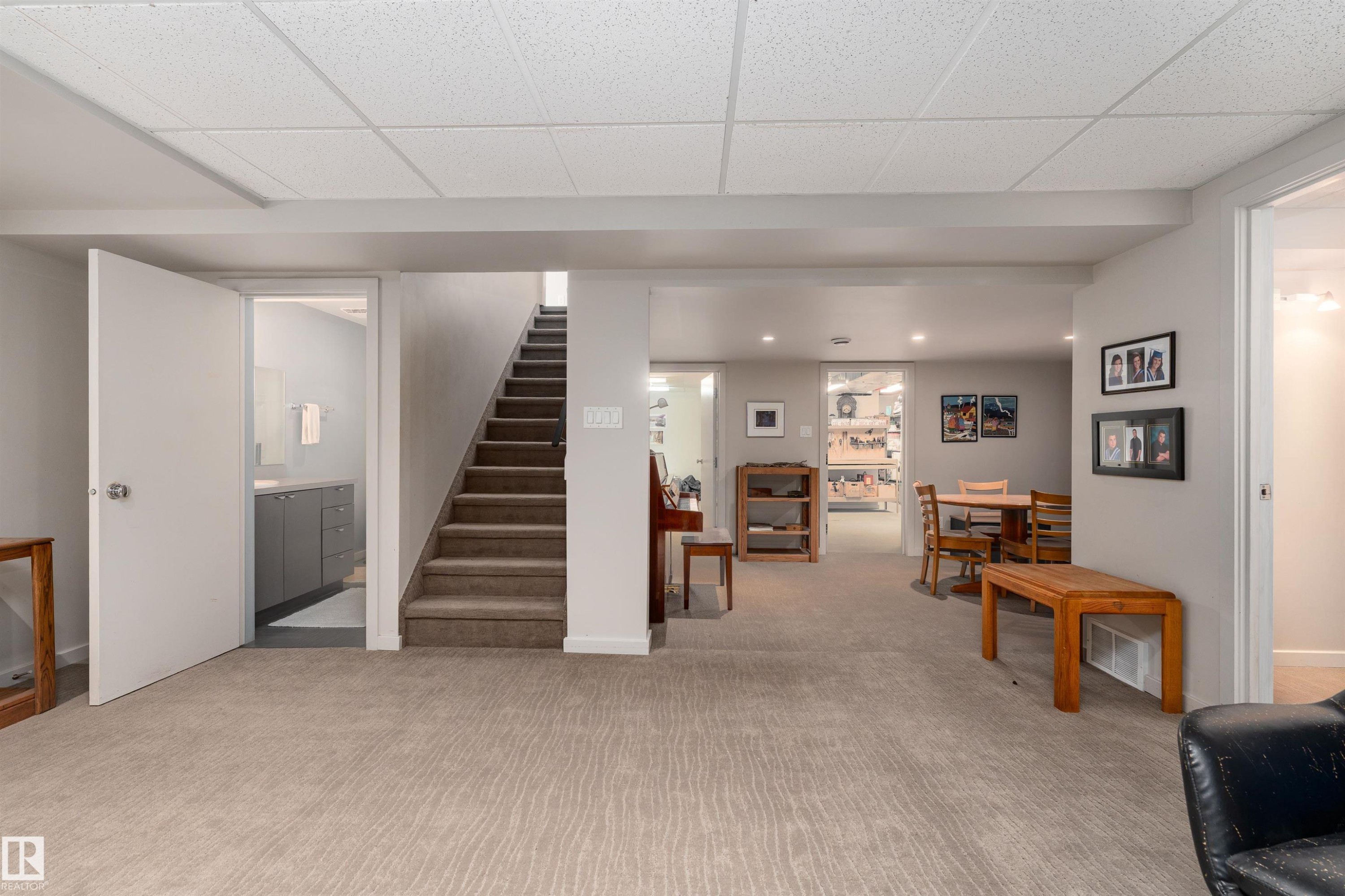 The property features a spacious room with light-colored carpet, a staircase with carpeted treads, and an open doorway leading to a bathroom with a vanity - 9715 141 Street Nw, Edmonton, AB - Indoor