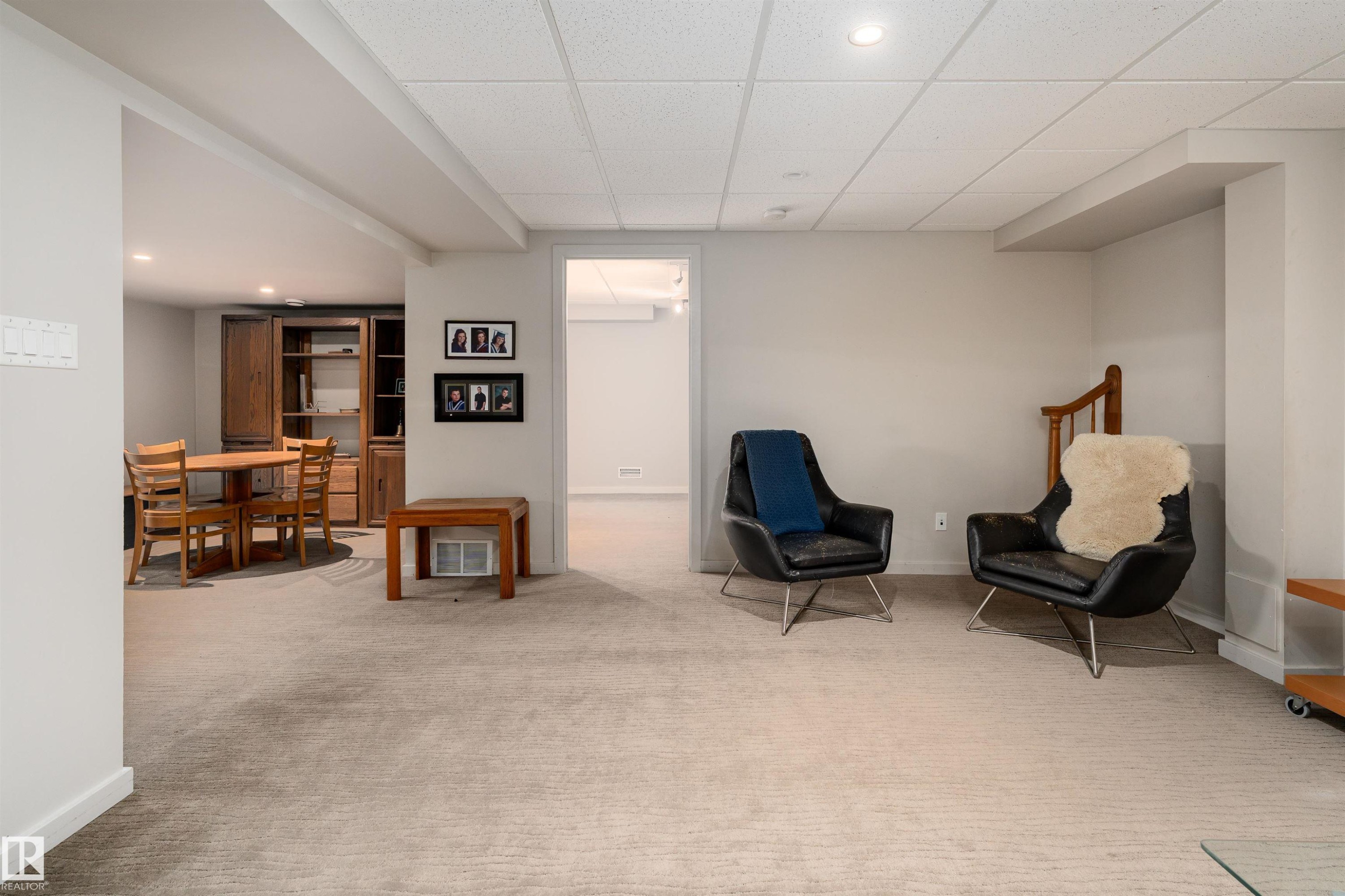The property features a spacious room with light-colored carpet, a drop ceiling with recessed lighting, and a wooden staircase - 9715 141 Street Nw, Edmonton, AB - Indoor