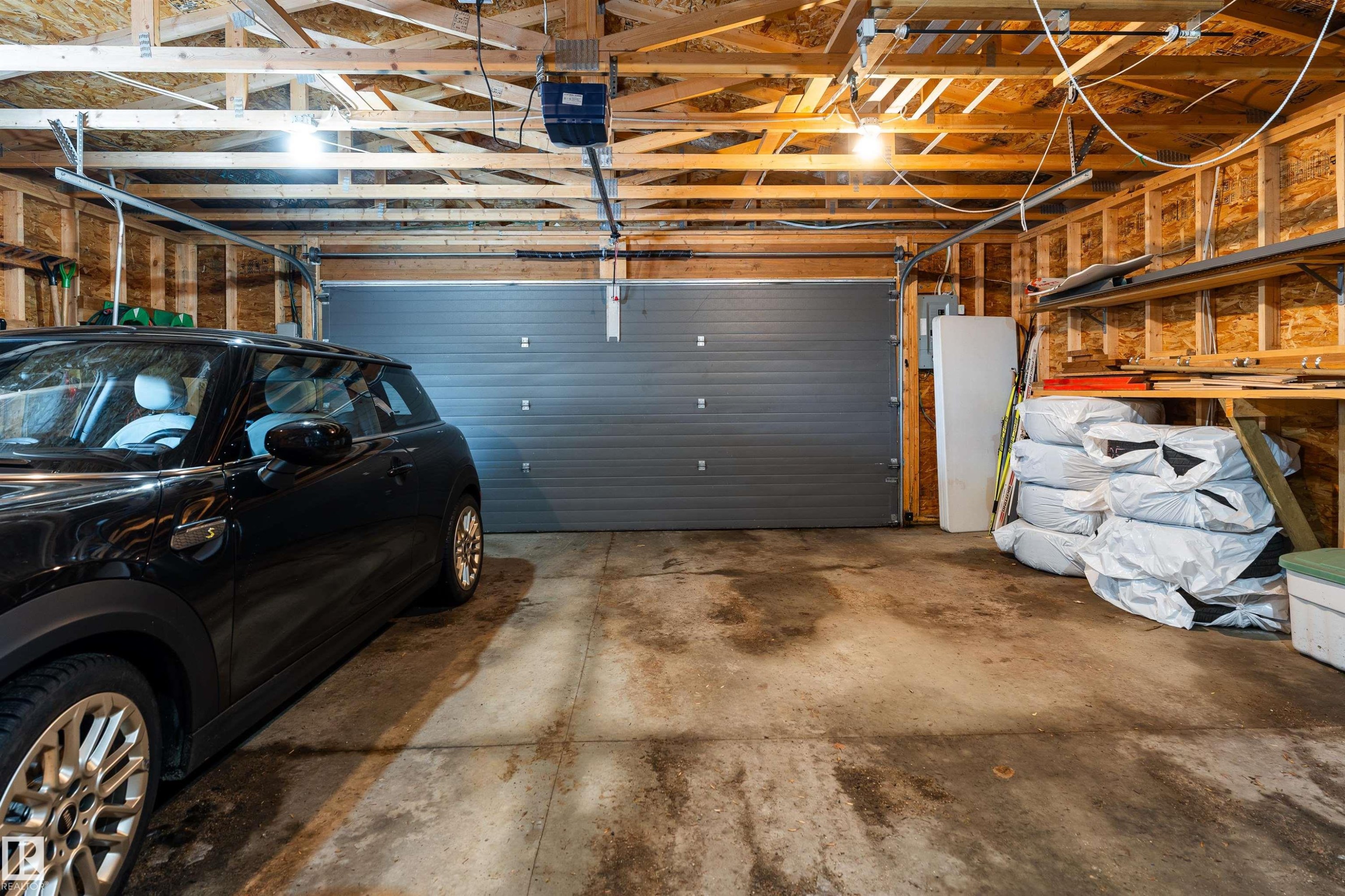 The property features a garage with exposed wooden beams, a gray sectional garage door, and built-in wooden shelving for storage - 9715 141 Street Nw, Edmonton, AB - Indoor Photo Showing Garage