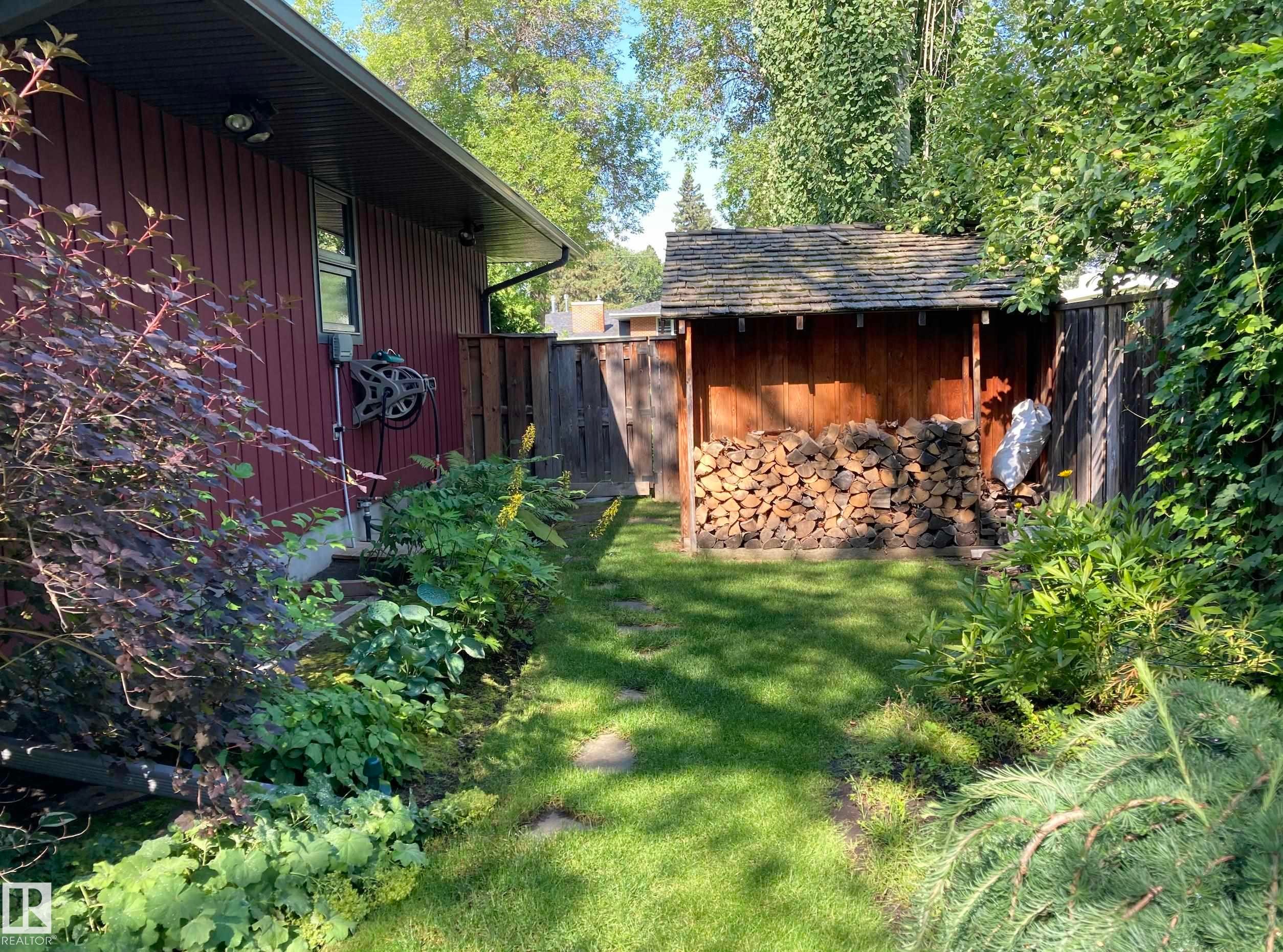 The property features a well-maintained lawn with stepping stones, bordered by various plantings - 9715 141 Street Nw, Edmonton, AB - Outdoor