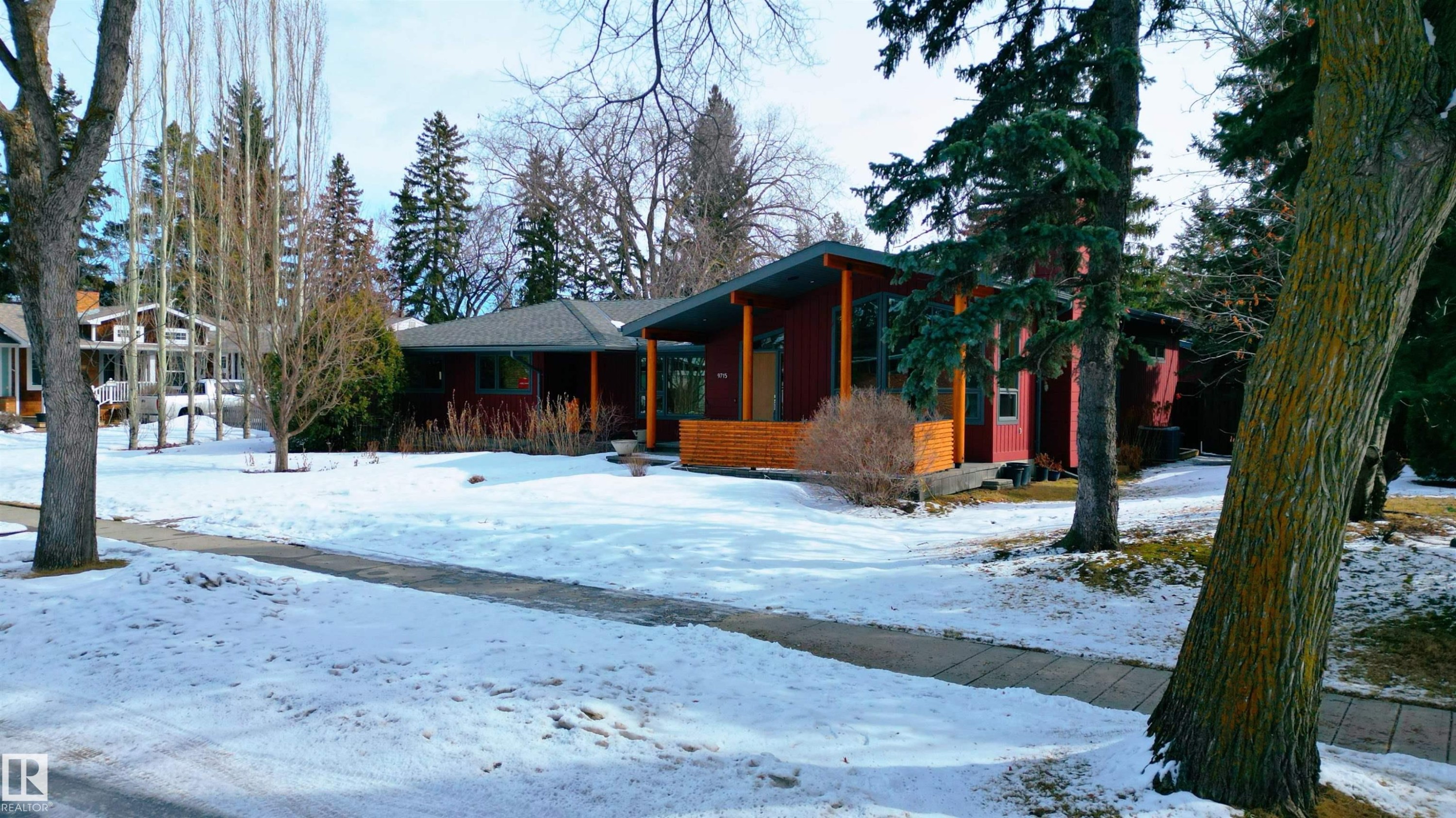 The property features a modern ranch-style home with a dark red exterior, a gray roof, and a wooden porch - 9715 141 Street Nw, Edmonton, AB - Outdoor