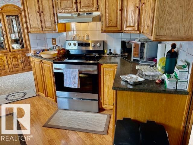 The kitchen features wood cabinetry, a stainless steel range with an overhead microwave, and a tiled backsplash - 4809 53 Ave, Willingdon, AB - Indoor Photo Showing Kitchen