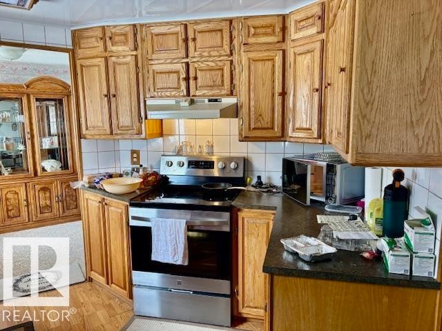 The kitchen features wood cabinetry, a tiled backsplash, and stainless steel appliances including a range and microwave - 4809 53 Ave, Willingdon, AB - Indoor Photo Showing Kitchen