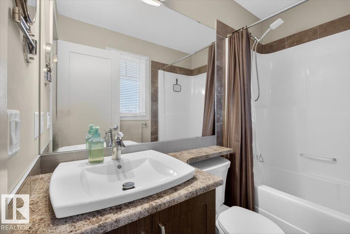 The bathroom features a vanity with a white vessel sink and a speckled countertop, a toilet, and a bathtub with a shower and a shower curtain - 16656 14 Avenue, Edmonton, AB - Indoor Photo Showing Bathroom