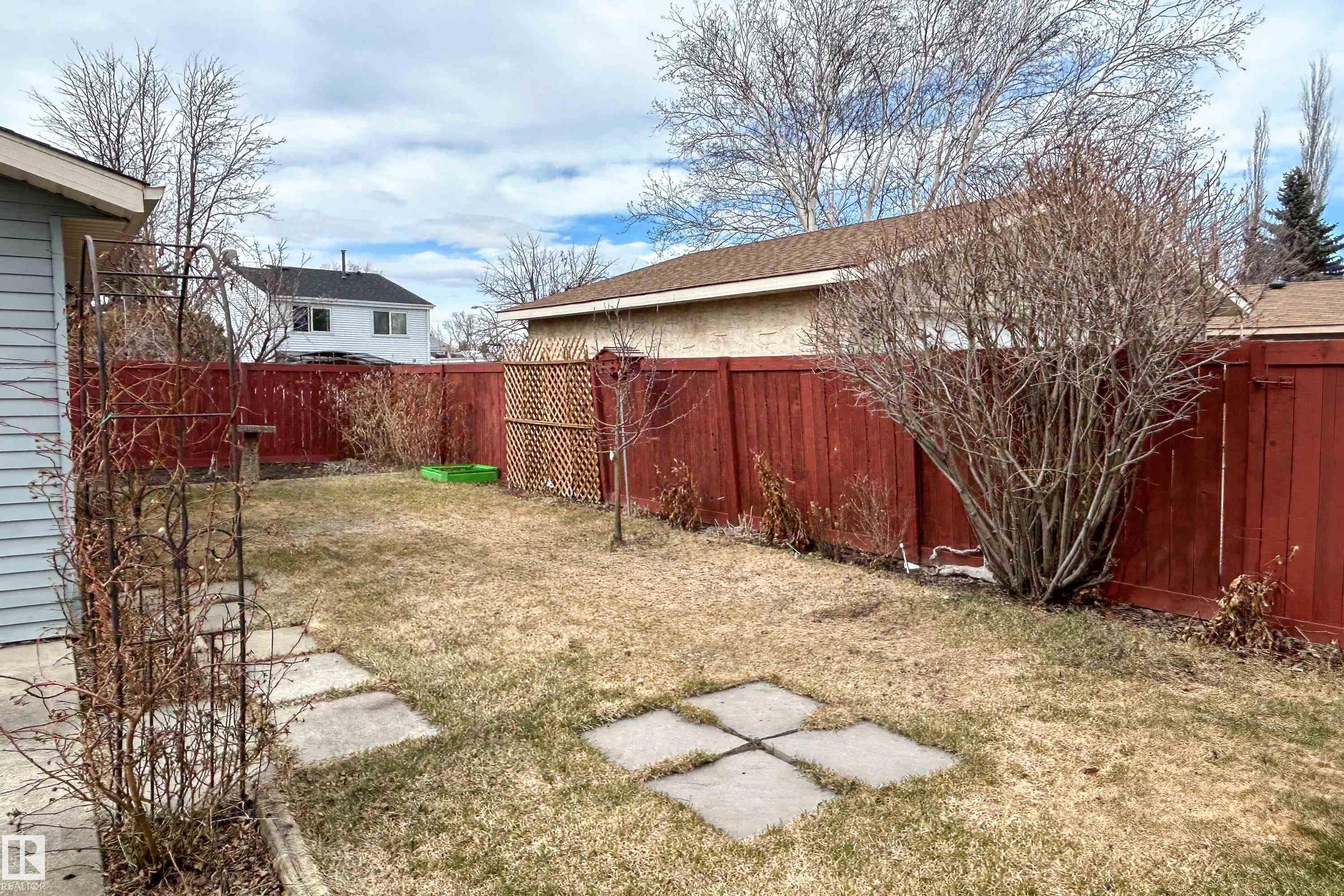 Fenced backyard featuring a lawn area, concrete stepping stones, a decorative metal arbor, and mature landscaping - 1104 35 Street, Edmonton, AB - Outdoor