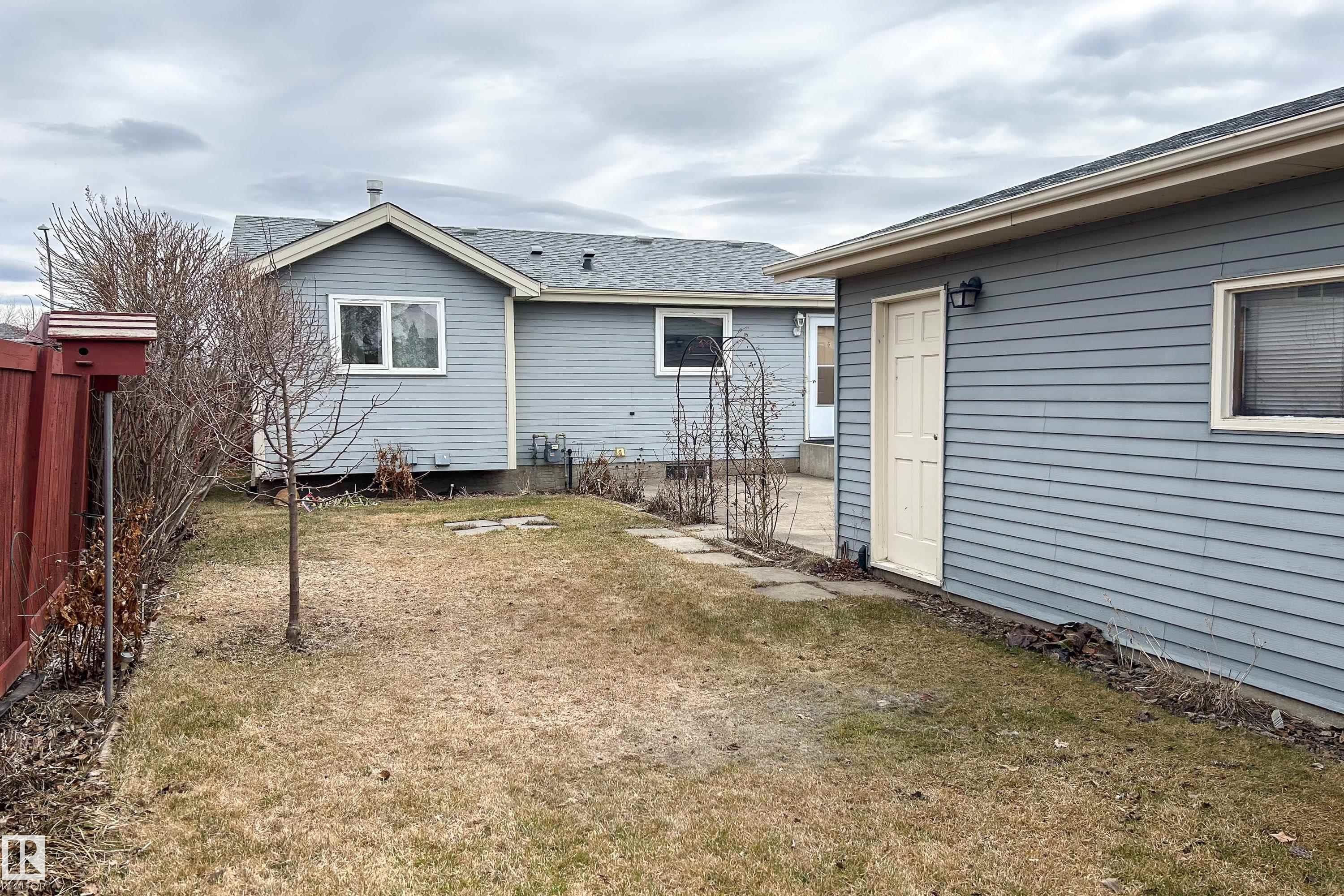 Expansive backyard featuring a red wood fence, a small tree, and a stone path leading to an outbuilding with horizontal siding, an exterior light fixture, and a white door - 1104 35 Street, Edmonton, AB - Outdoor