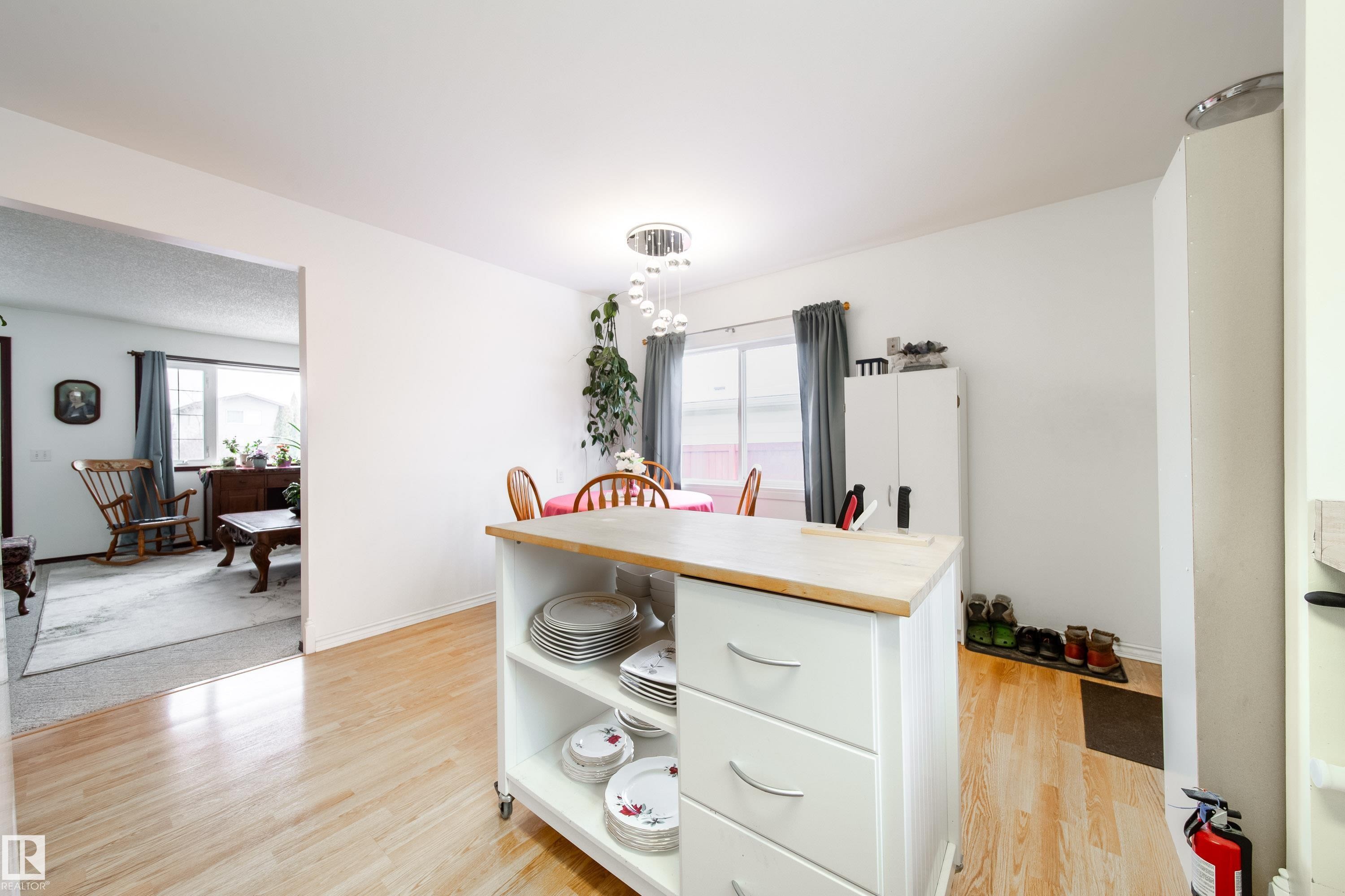 The property features light-toned hardwood flooring in the dining area, with an overhead light fixture, and a window with curtains - 1104 35 Street, Edmonton, AB - Indoor