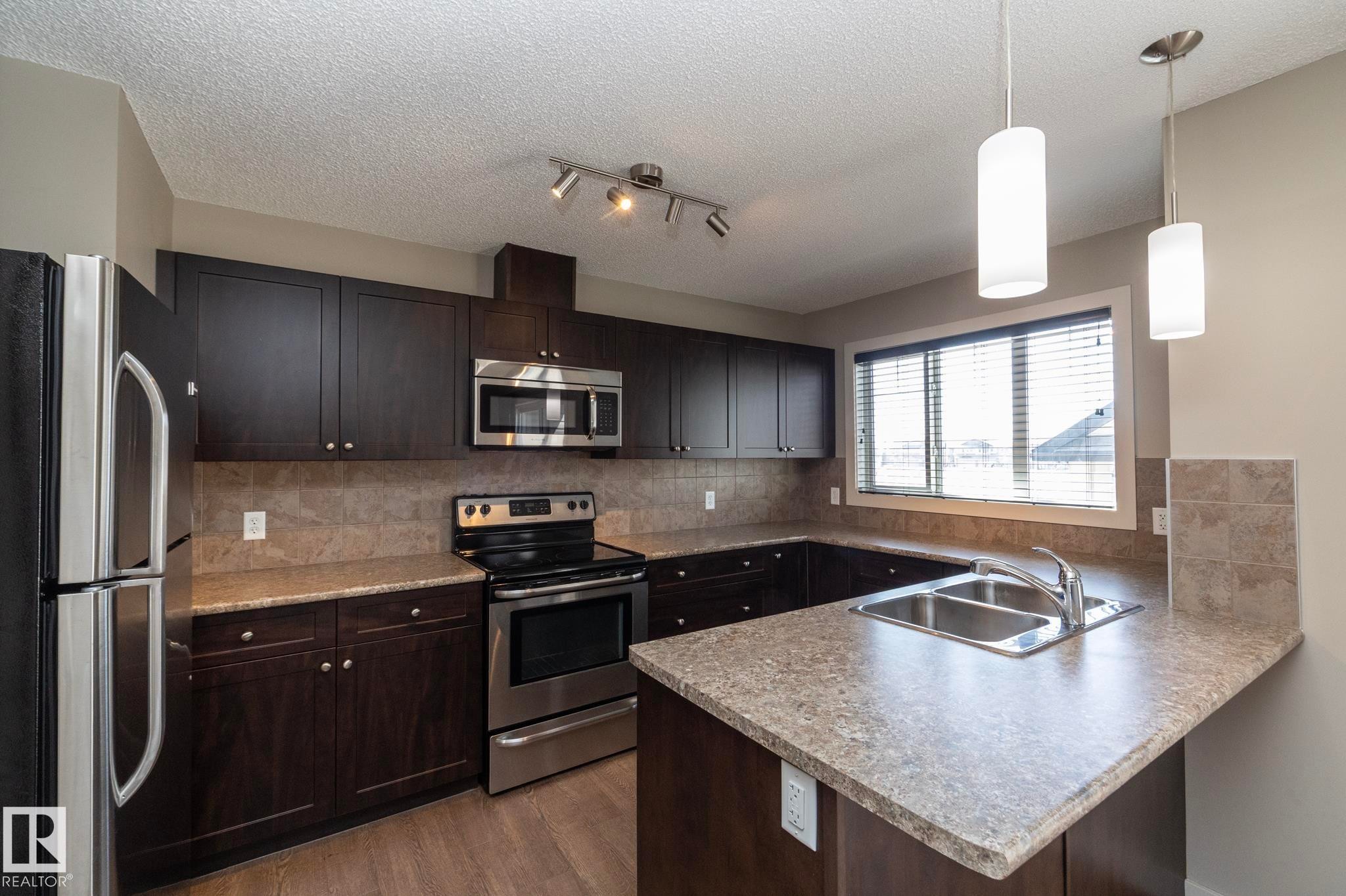 The kitchen features dark wood cabinetry, stainless steel appliances, a double basin sink, and pendant lighting - 1403 Cunningham Drive, Edmonton, AB - Indoor Photo Showing Kitchen With Double Sink