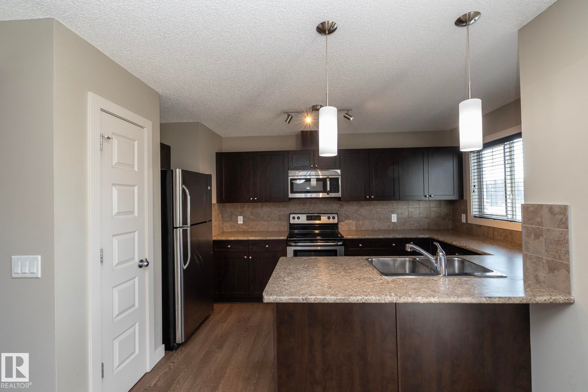 The kitchen features dark wood cabinetry, a double basin stainless steel sink, and light-colored countertops - 1403 Cunningham Drive, Edmonton, AB - Indoor Photo Showing Kitchen With Double Sink