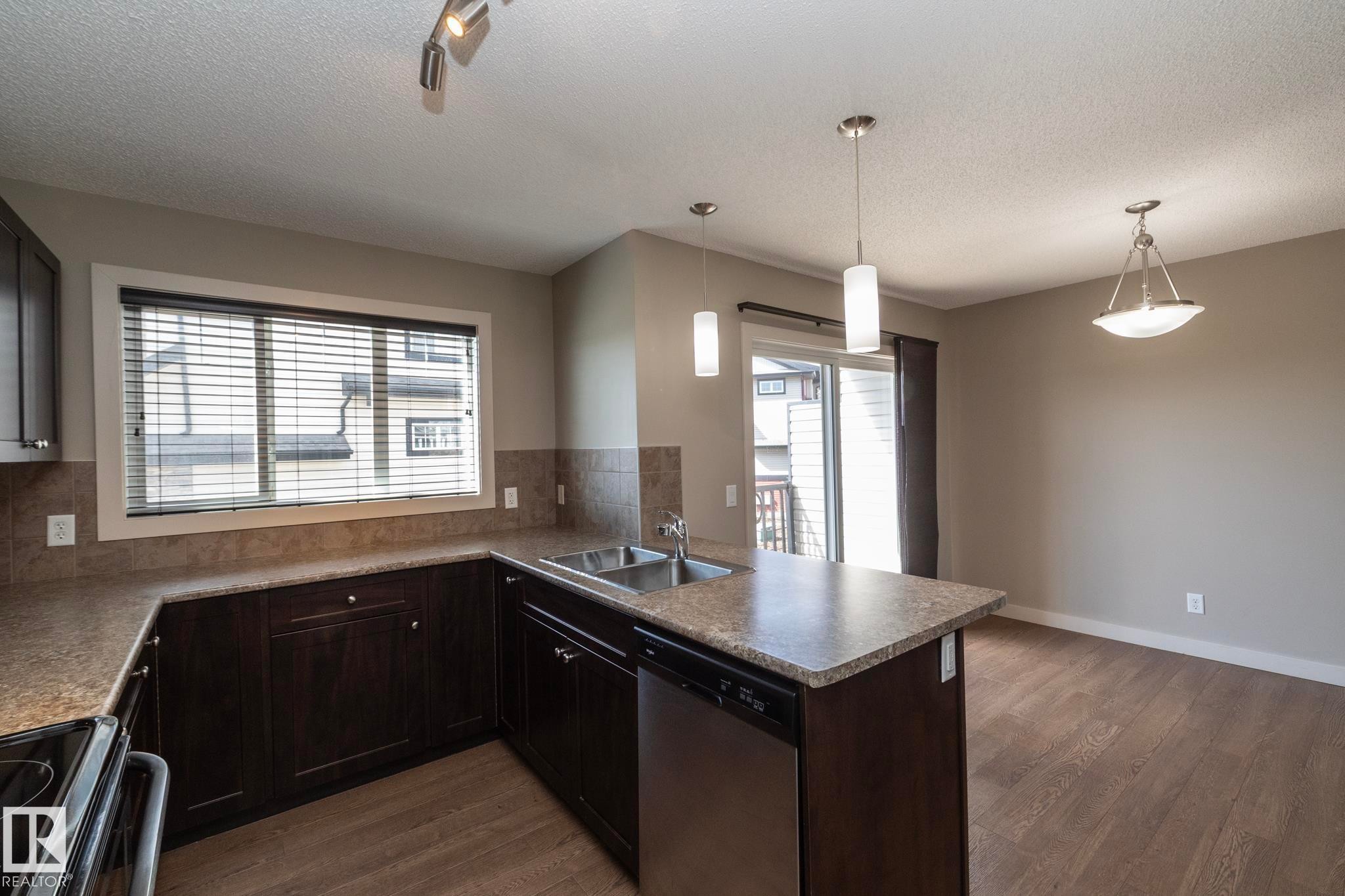 The kitchen features dark wood cabinetry, a double basin sink, and stainless steel appliances - 1403 Cunningham Drive, Edmonton, AB - Indoor Photo Showing Kitchen With Double Sink
