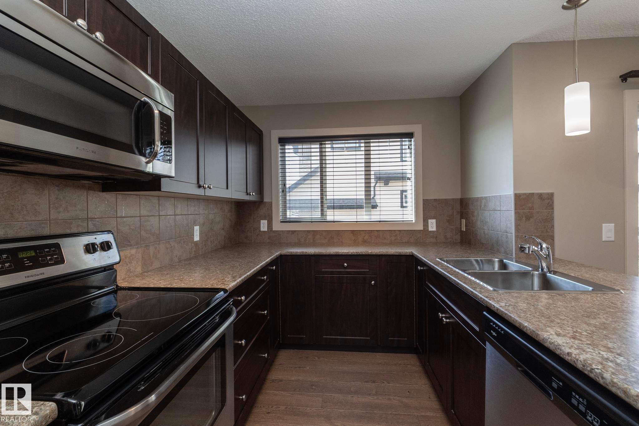 The kitchen features dark wood cabinetry, stainless steel appliances, a double sink, and a tiled backsplash - 1403 Cunningham Drive, Edmonton, AB - Indoor Photo Showing Kitchen With Double Sink