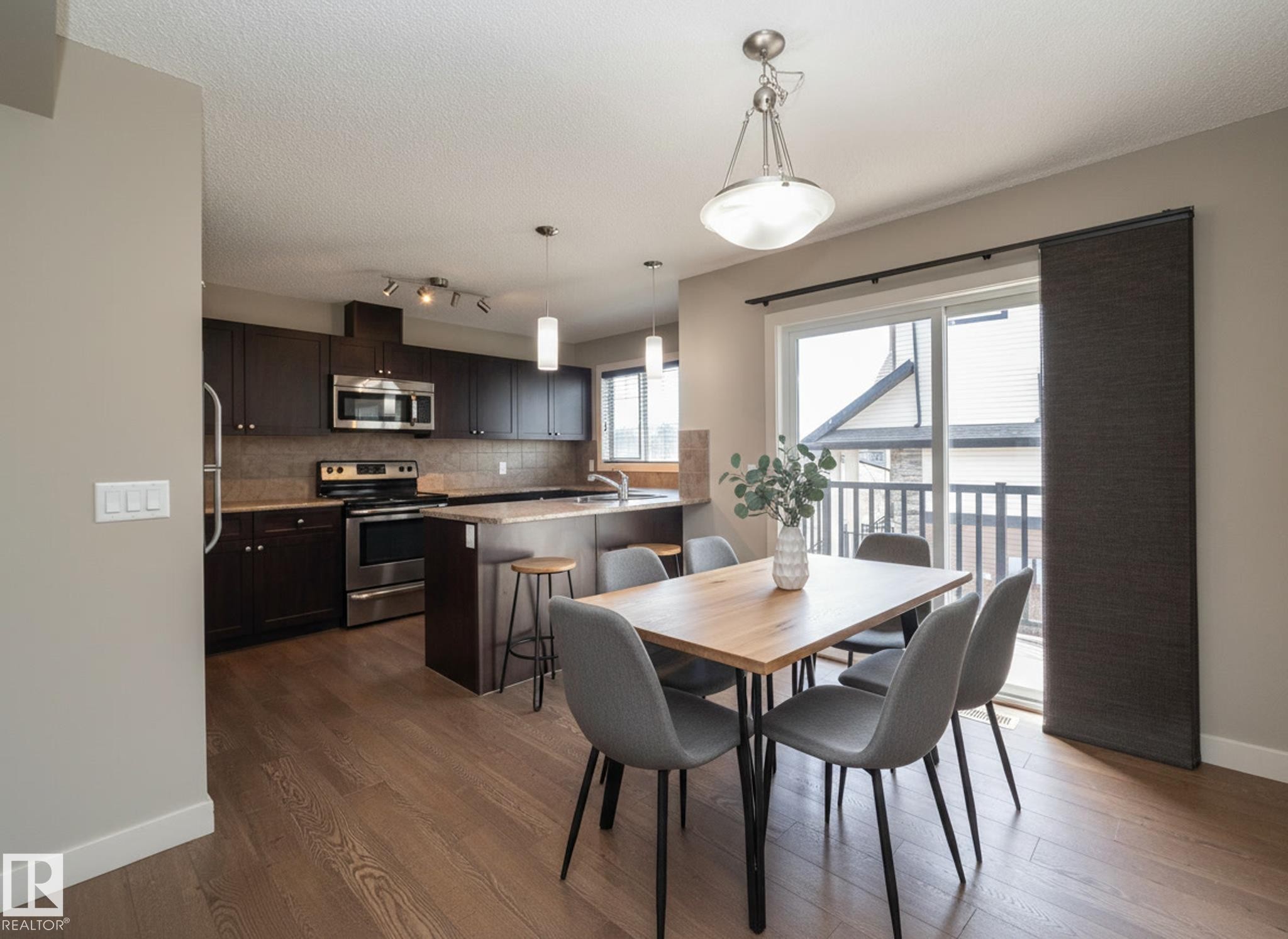 This open-concept dining area features hardwood floors and a sliding glass door - 1403 Cunningham Drive, Edmonton, AB - Indoor Photo Showing Dining Room