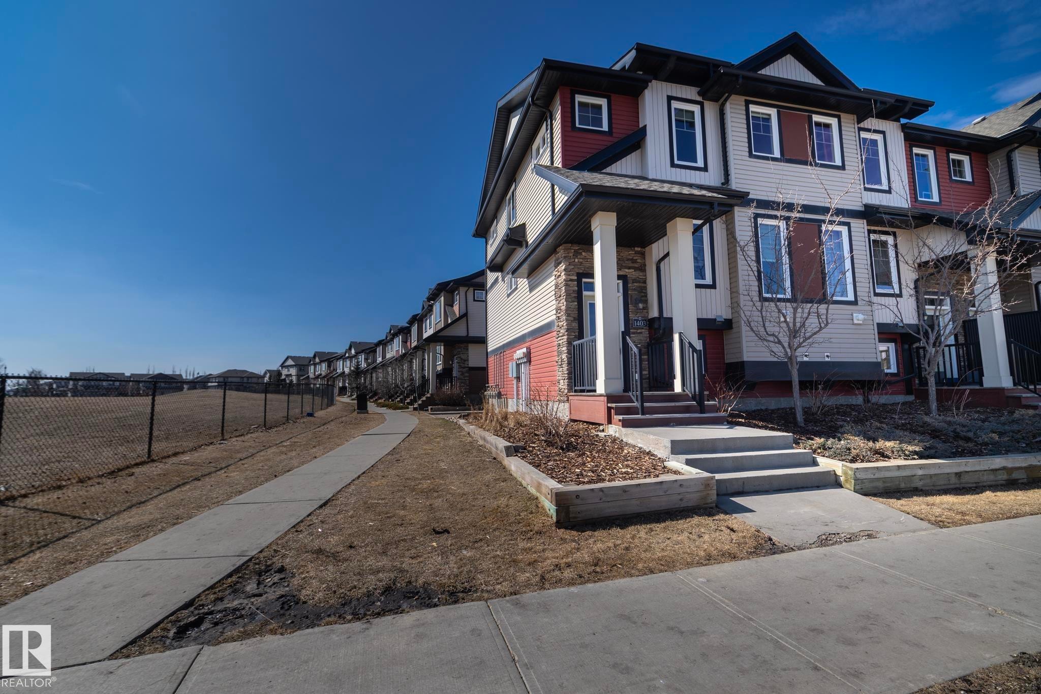 The property features a multi-story exterior with red and beige siding, white trim, and a prominent front entrance with steps and a porch supported by columns - 1403 Cunningham Drive, Edmonton, AB - Outdoor With Facade