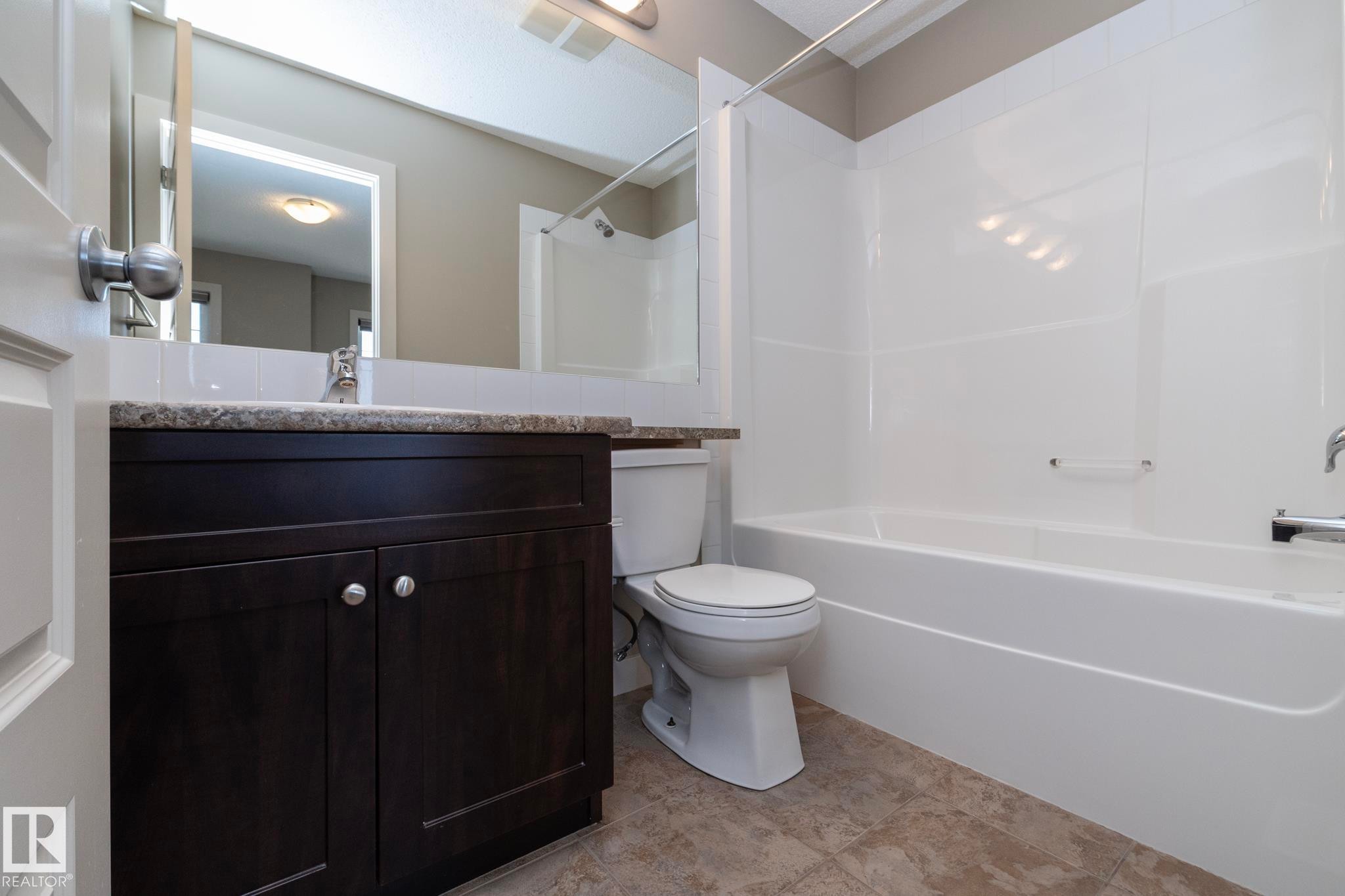 The bathroom features a dark wood vanity with a speckled countertop, a toilet, and a white bathtub with a shower - 1403 Cunningham Drive, Edmonton, AB - Indoor Photo Showing Bathroom