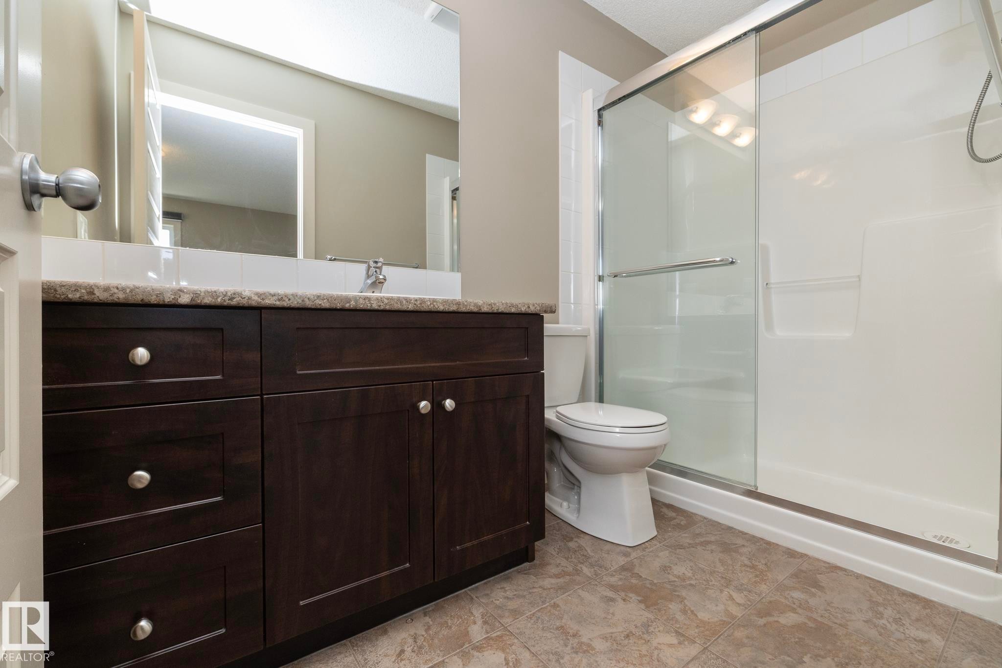 Bathroom featuring a dark wood vanity with a light-colored countertop, a shower with a sliding glass door, and neutral-toned floor tiles - 1403 Cunningham Drive, Edmonton, AB - Indoor Photo Showing Bathroom