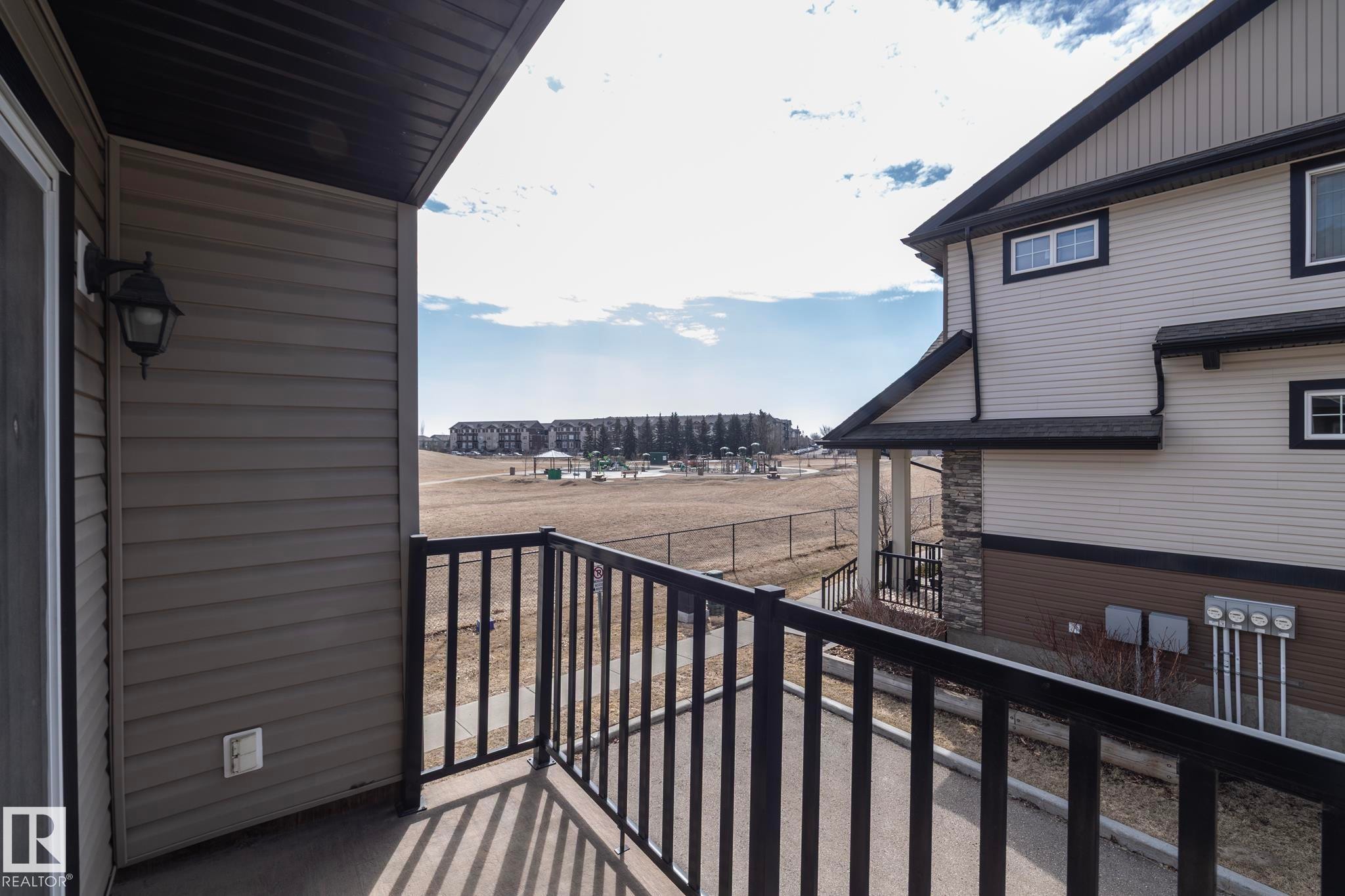 The property includes a private balcony with black railings, offering views of a fenced-in field and distant buildings - 1403 Cunningham Drive, Edmonton, AB - Outdoor With Exterior
