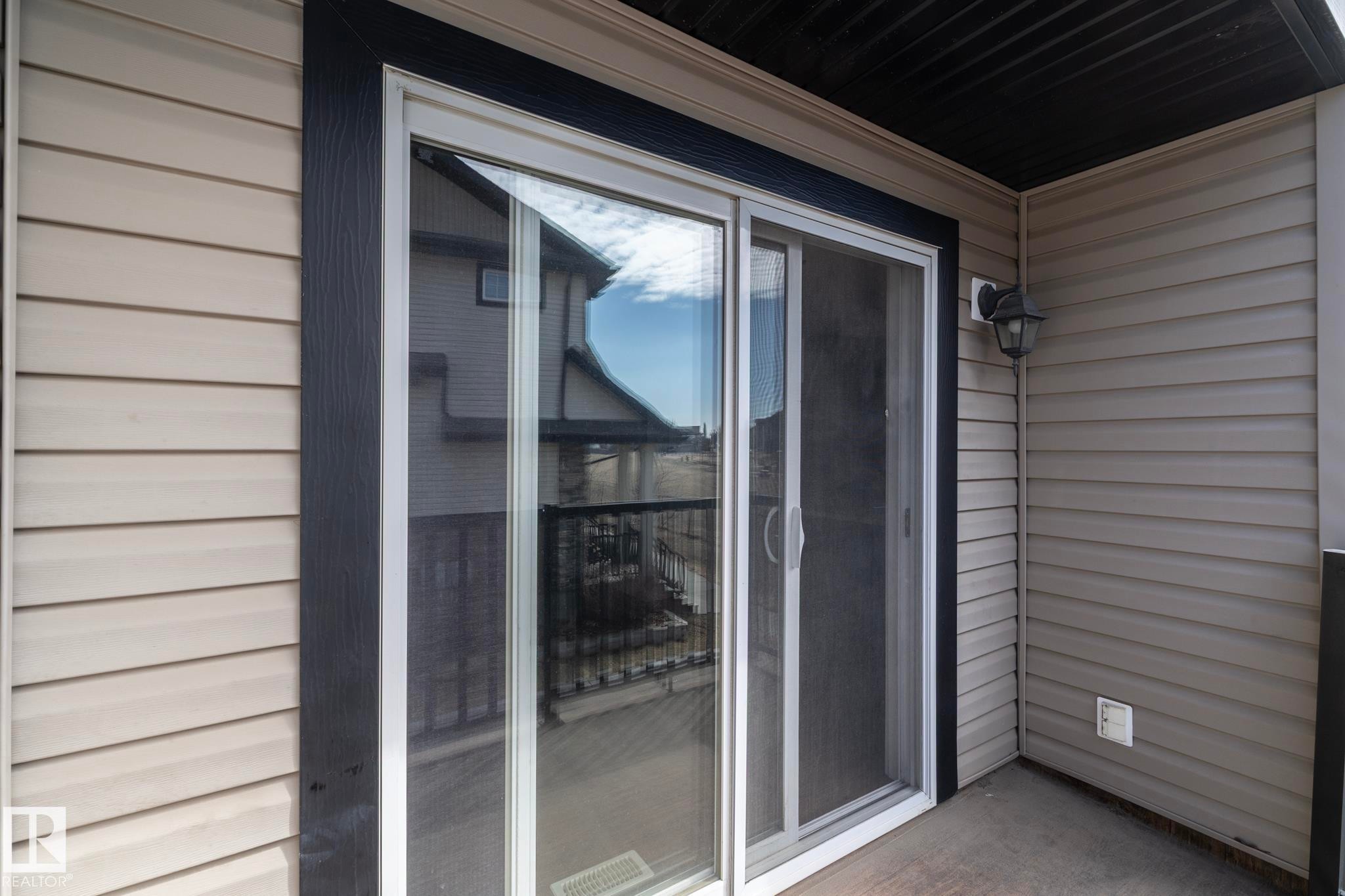 The property features a sliding glass door with a screen, opening onto a balcony with composite siding and an exterior light fixture - 1403 Cunningham Drive, Edmonton, AB - Outdoor With Exterior