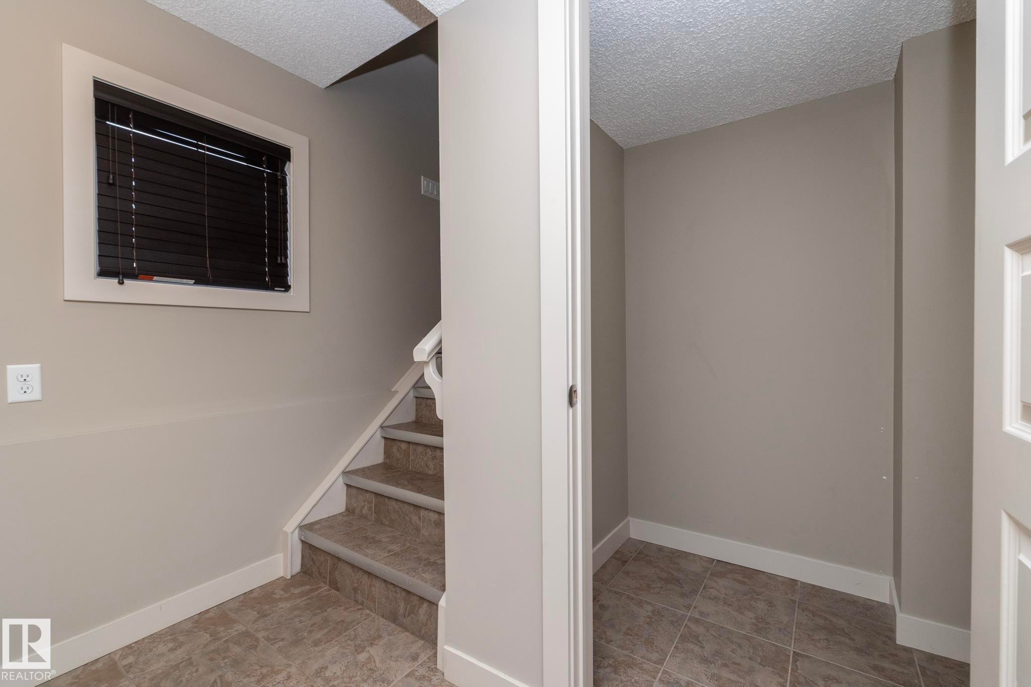 The property features a staircase with carpeted treads and a window with blinds - 1403 Cunningham Drive, Edmonton, AB - Indoor Photo Showing Other Room