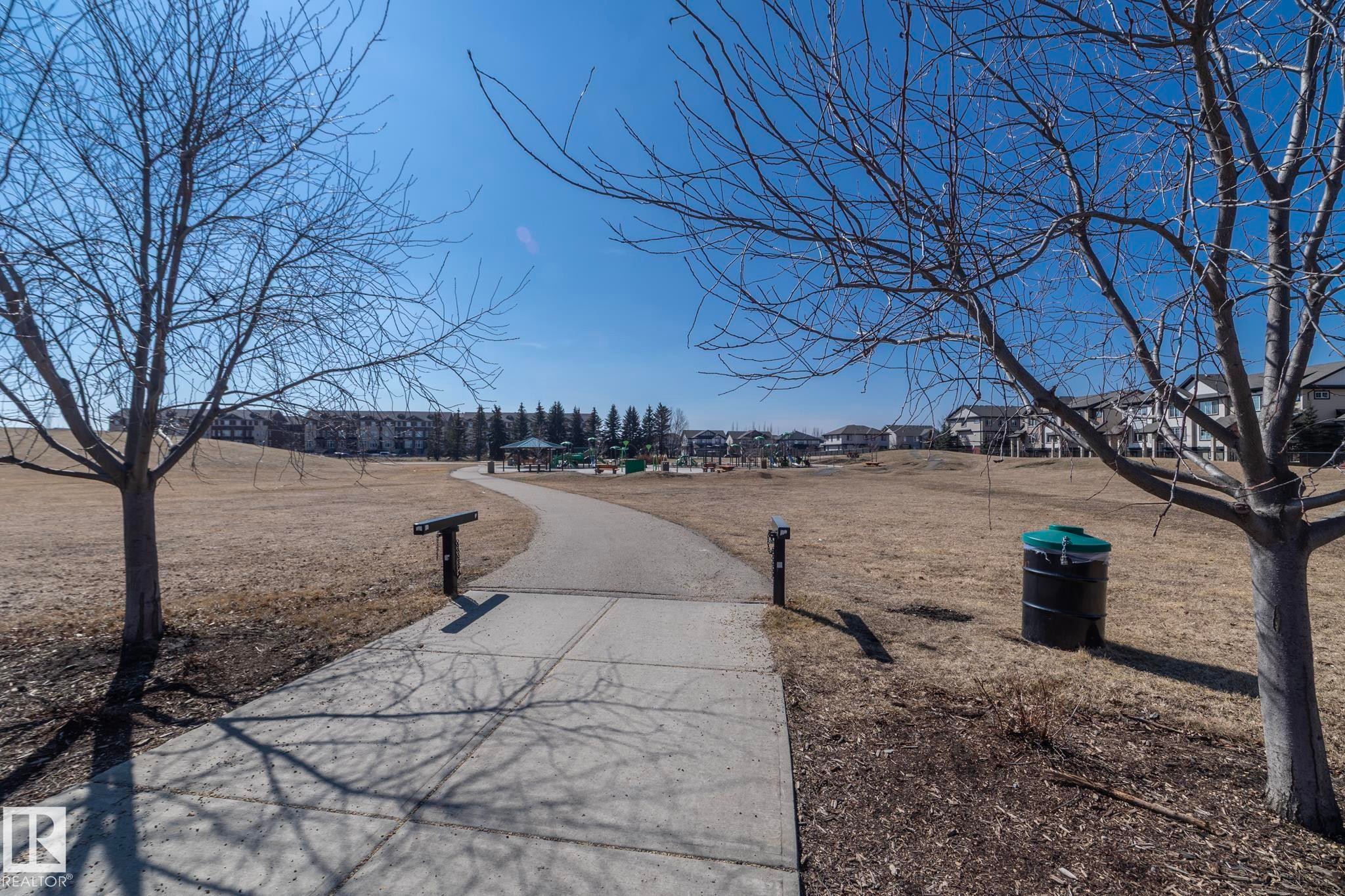 Community green space featuring a paved pathway, mature trees, and nearby residential buildings - 1403 Cunningham Drive, Edmonton, AB - Outdoor With View