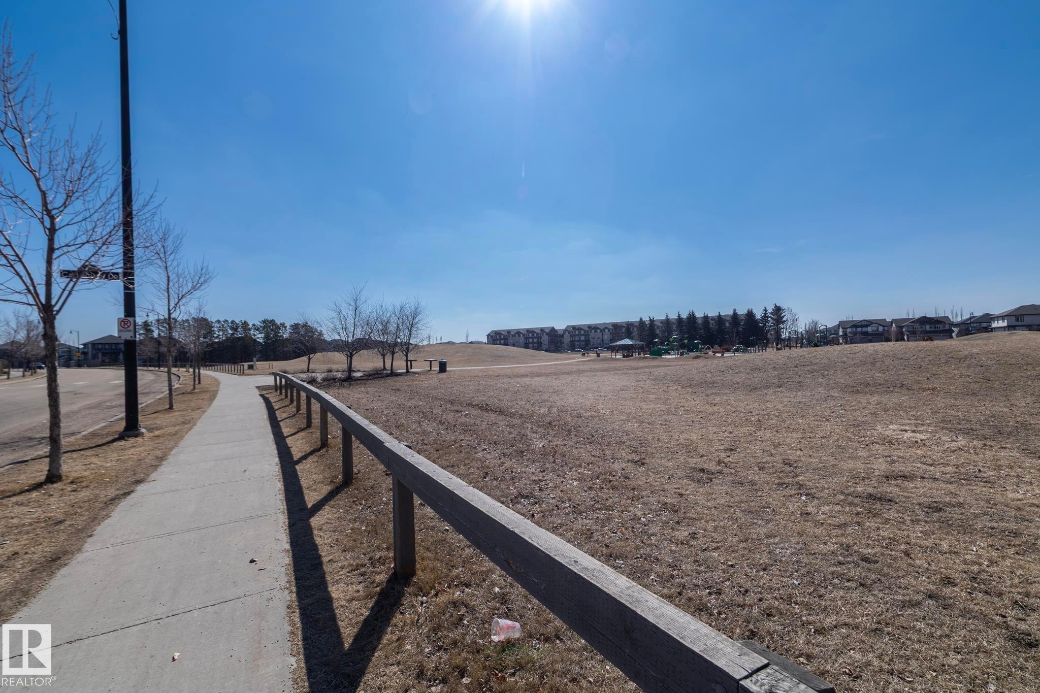 The property is situated within a community featuring a paved walking path, a large open field, and distant residential buildings - 1403 Cunningham Drive, Edmonton, AB - Outdoor With View