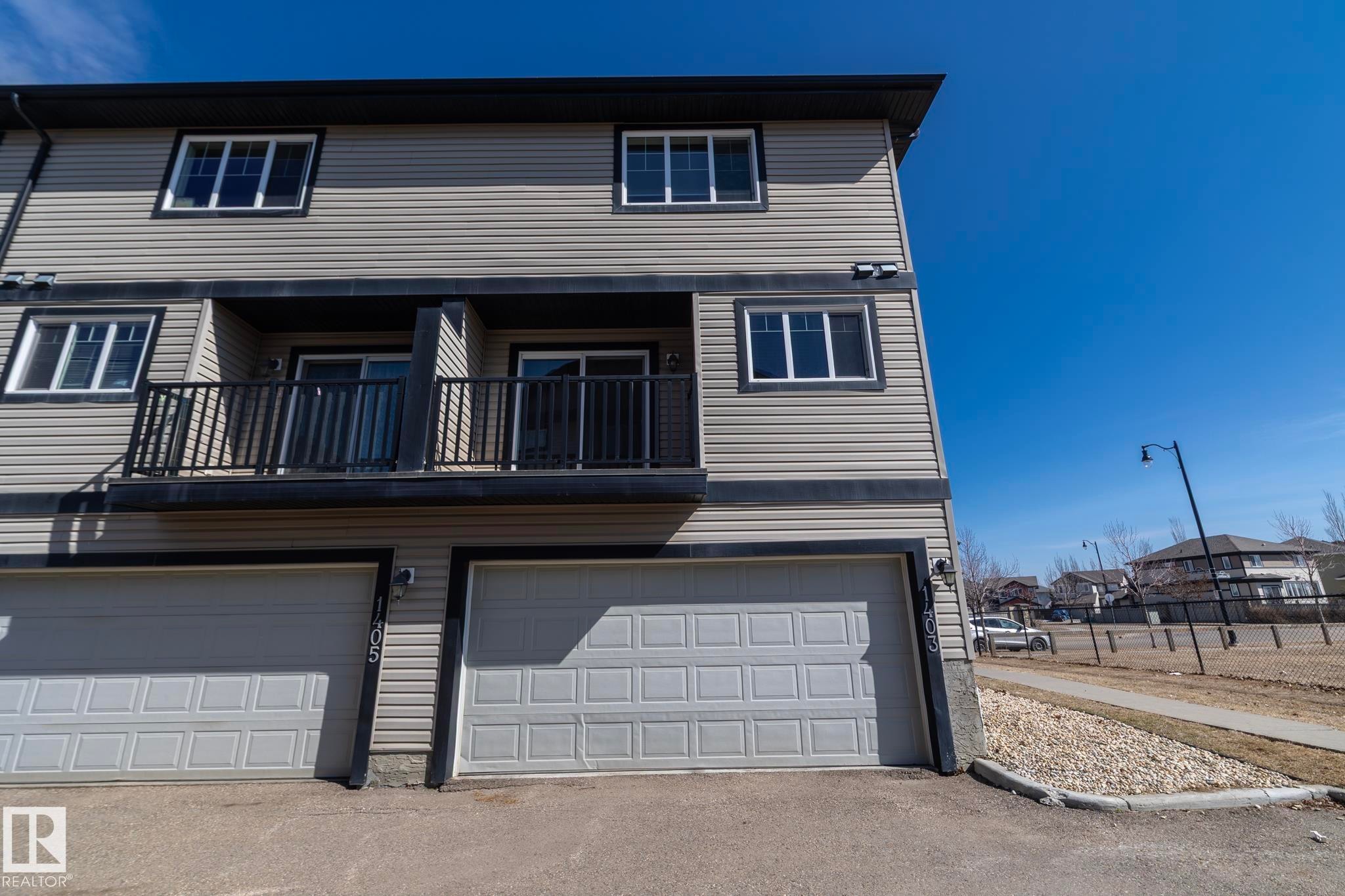 The property features a two-story exterior with horizontal siding, a balcony with black railings, and two garage doors - 1403 Cunningham Drive, Edmonton, AB - Outdoor