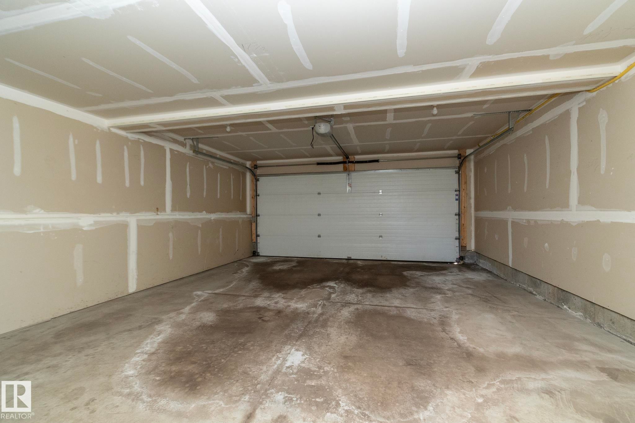 The property includes a garage with a concrete floor, a white garage door, and unfinished drywall on the walls and ceiling - 1403 Cunningham Drive, Edmonton, AB - Indoor Photo Showing Garage