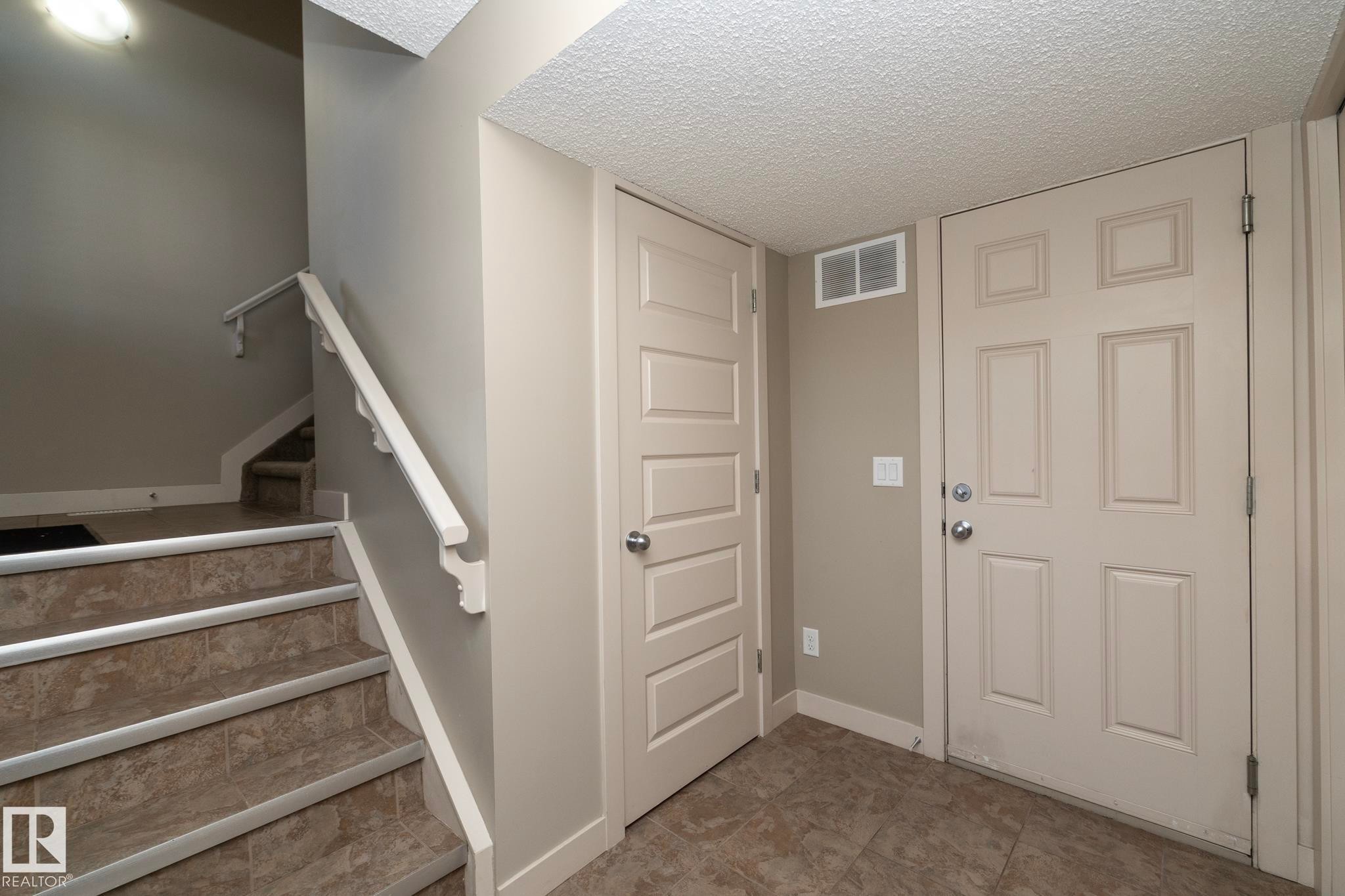 Entryway featuring a tiled floor, two paneled doors, and a staircase with tiled steps and a white handrail - 1403 Cunningham Drive, Edmonton, AB - Indoor Photo Showing Other Room