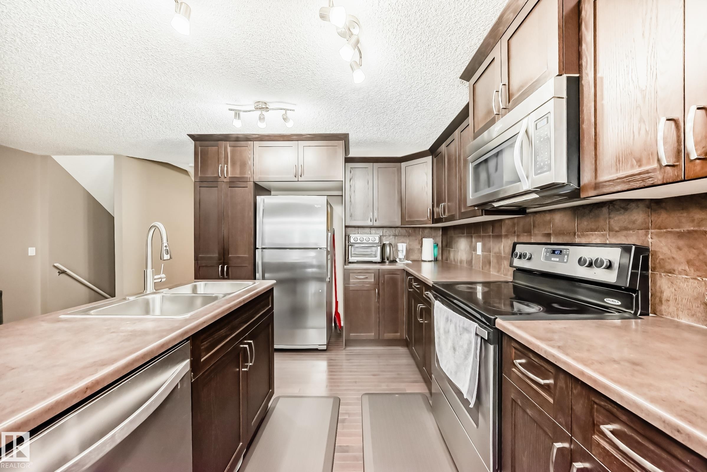 The kitchen features dark wood cabinetry, stainless steel appliances, and a double basin sink - 8 13838 166Ave, Edmonton, AB - Indoor Photo Showing Kitchen With Stainless Steel Kitchen With Double Sink With Upgraded Kitchen