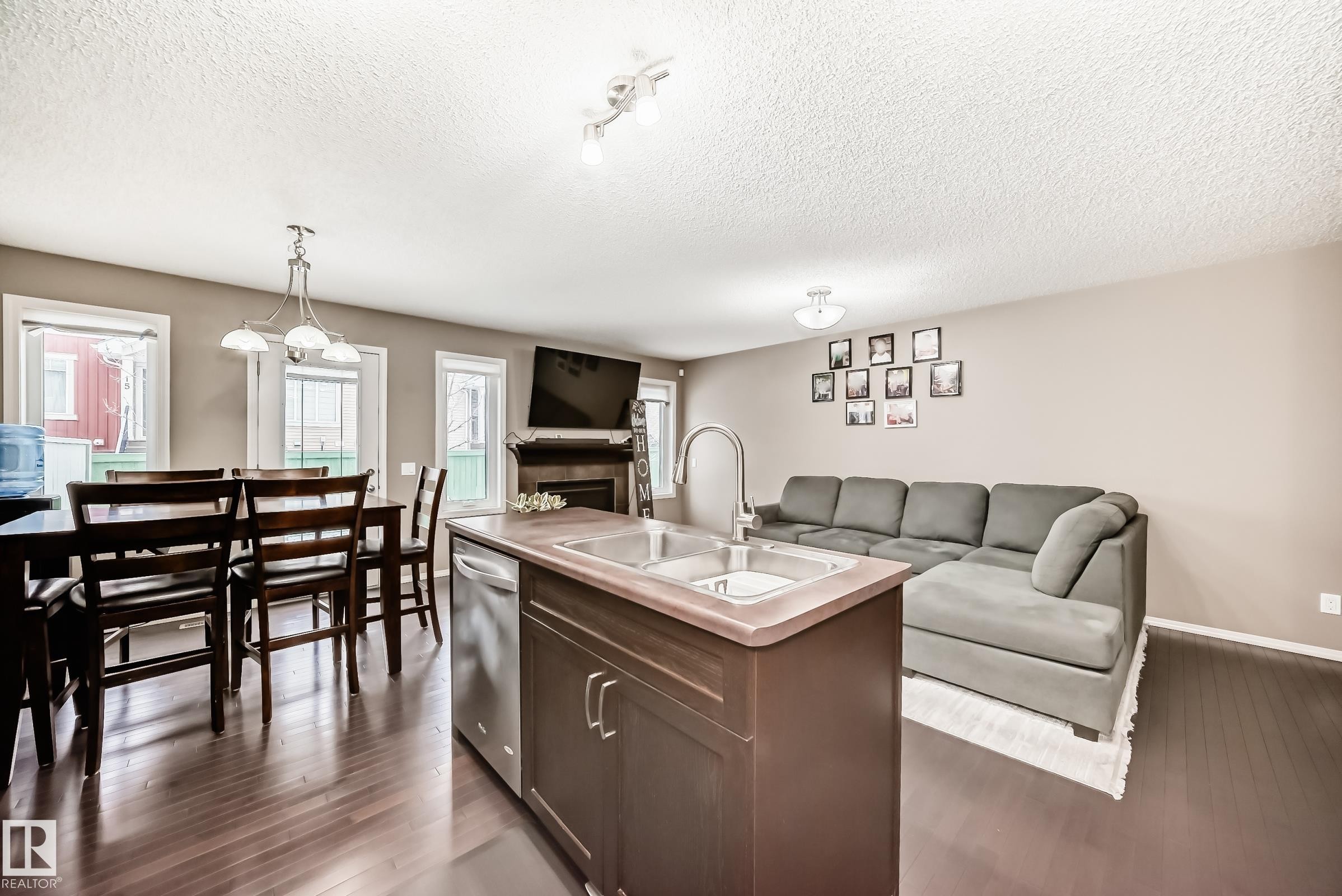 Open concept living space featuring dark hardwood flooring, a central kitchen island with a sink and dishwasher, and a dining area with a chandelier - 8 13838 166Ave, Edmonton, AB - Indoor