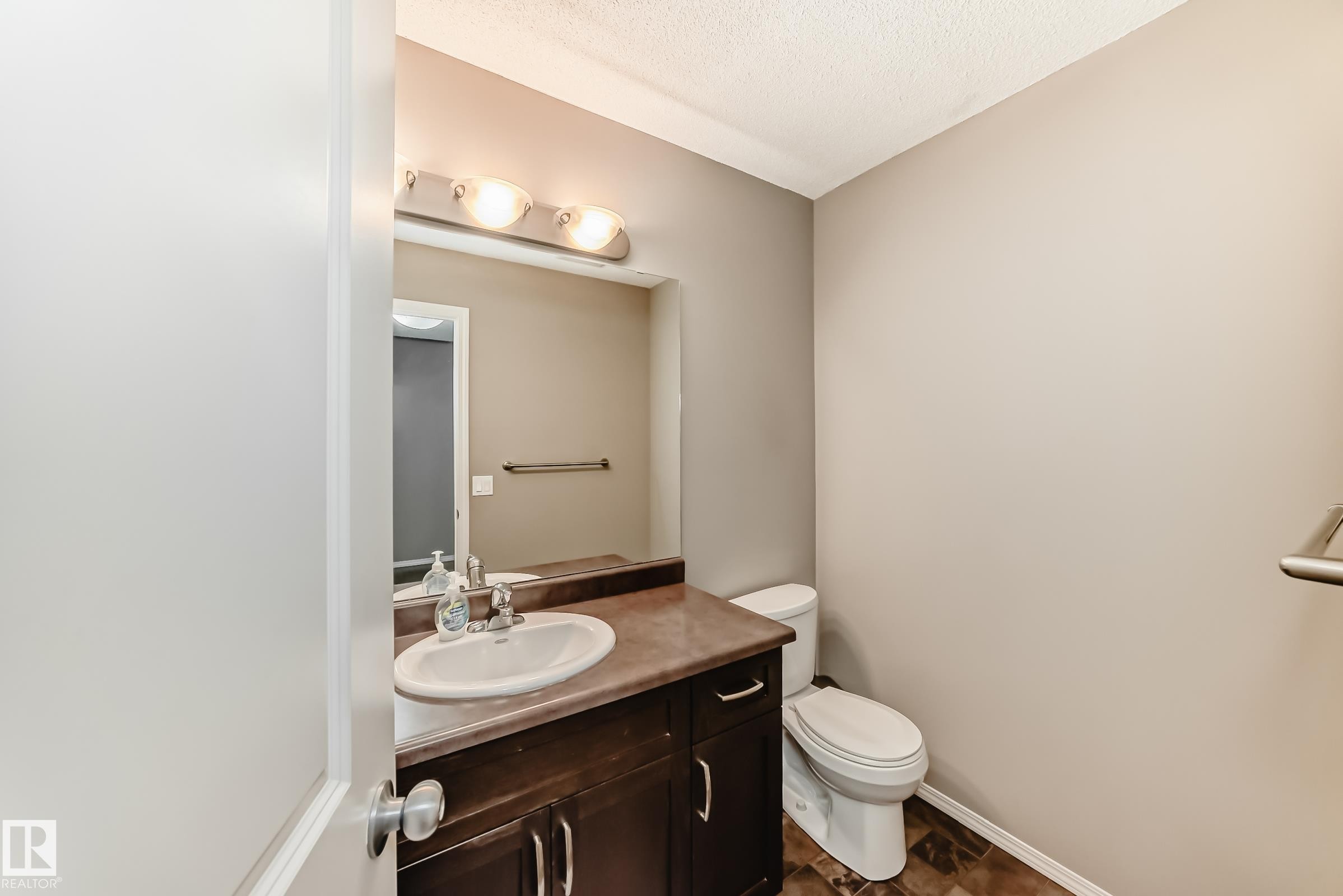The bathroom features a vanity with a sink, a mirror, and a toilet - 8 13838 166Ave, Edmonton, AB - Indoor Photo Showing Bathroom