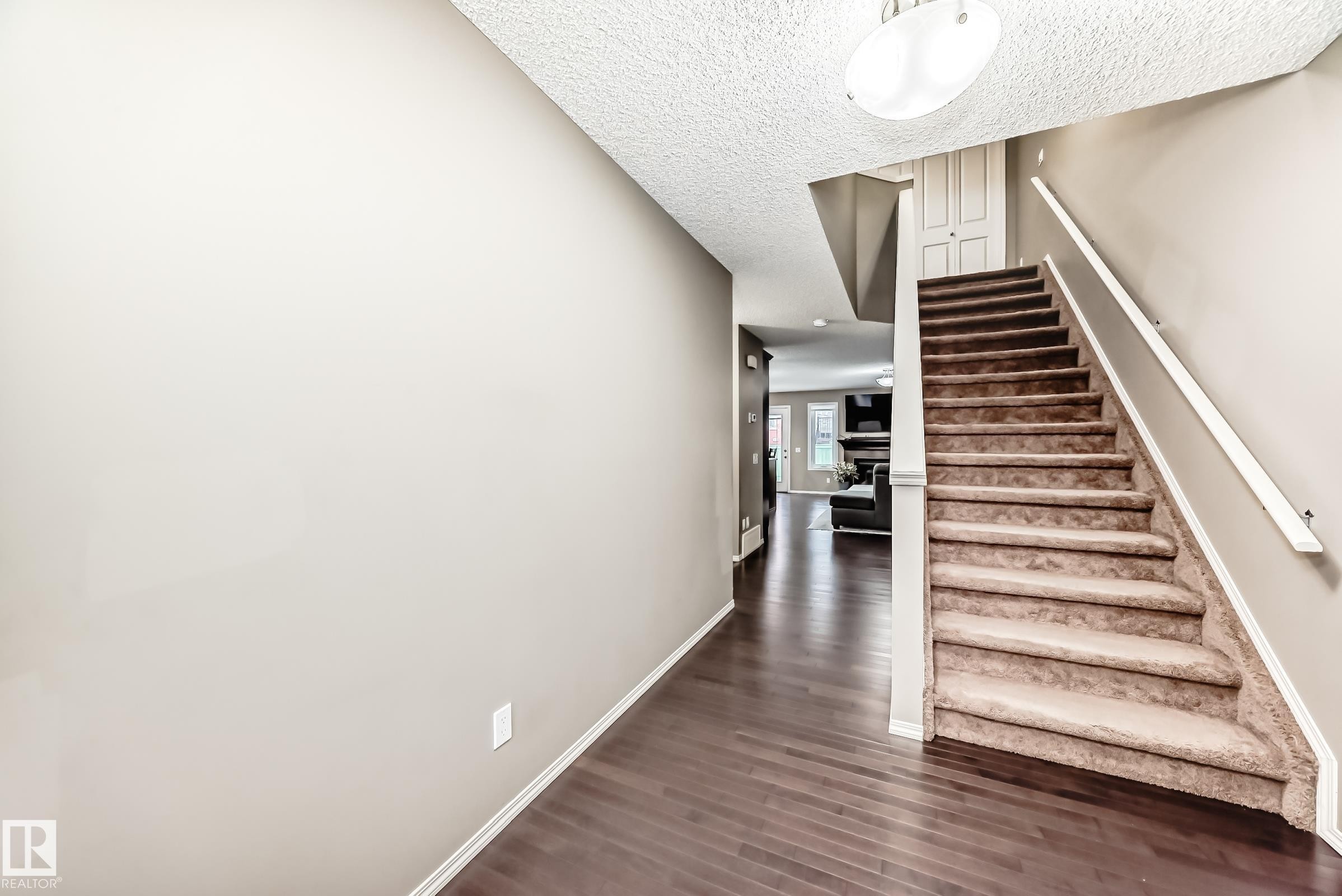 Entryway featuring dark hardwood flooring, a carpeted staircase with a white handrail, and a flush mount light fixture - 8 13838 166Ave, Edmonton, AB - Indoor Photo Showing Other Room