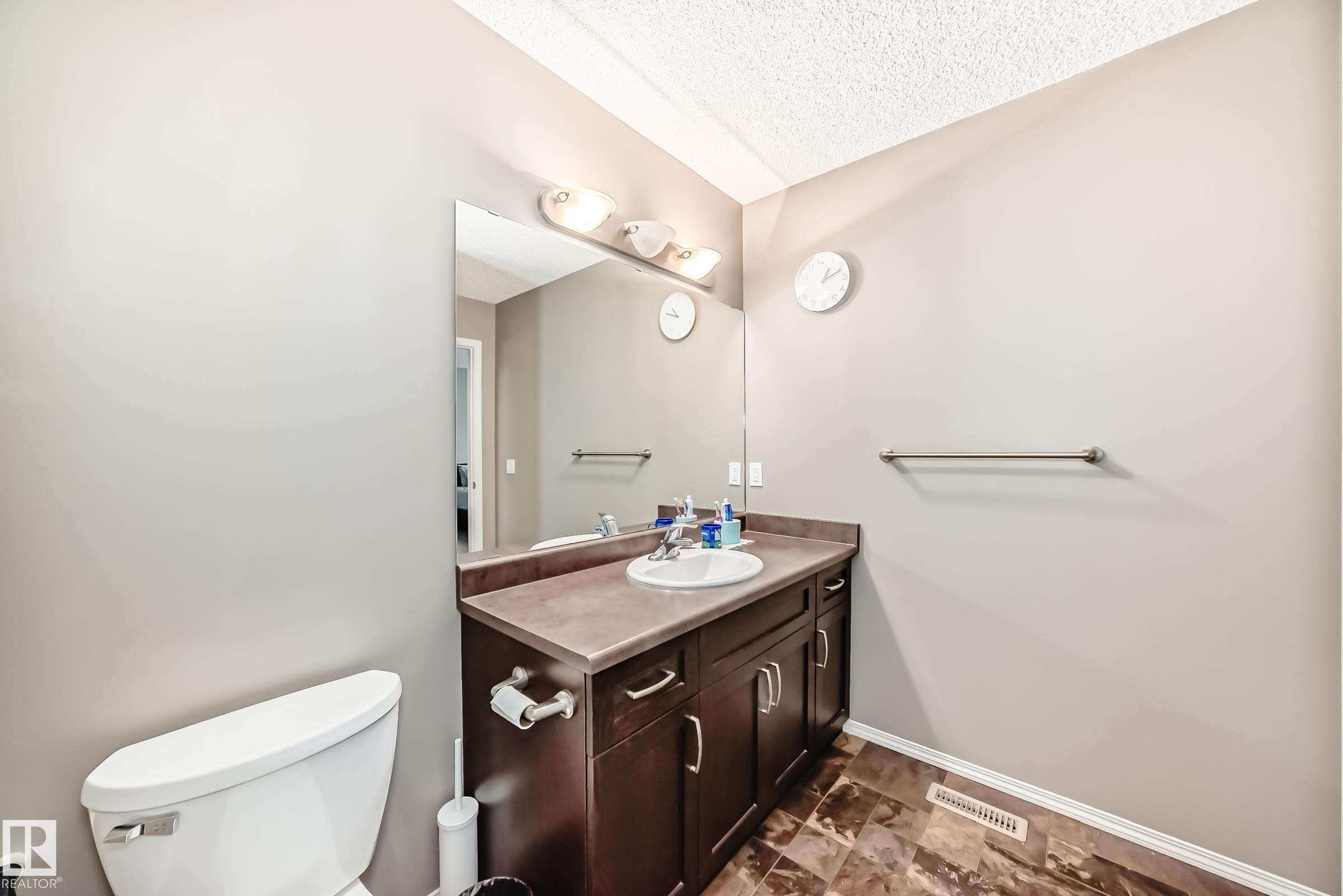 The bathroom features a vanity with dark wood cabinetry, a white basin, and a wall-mounted mirror - 8 13838 166Ave, Edmonton, AB - Indoor Photo Showing Bathroom