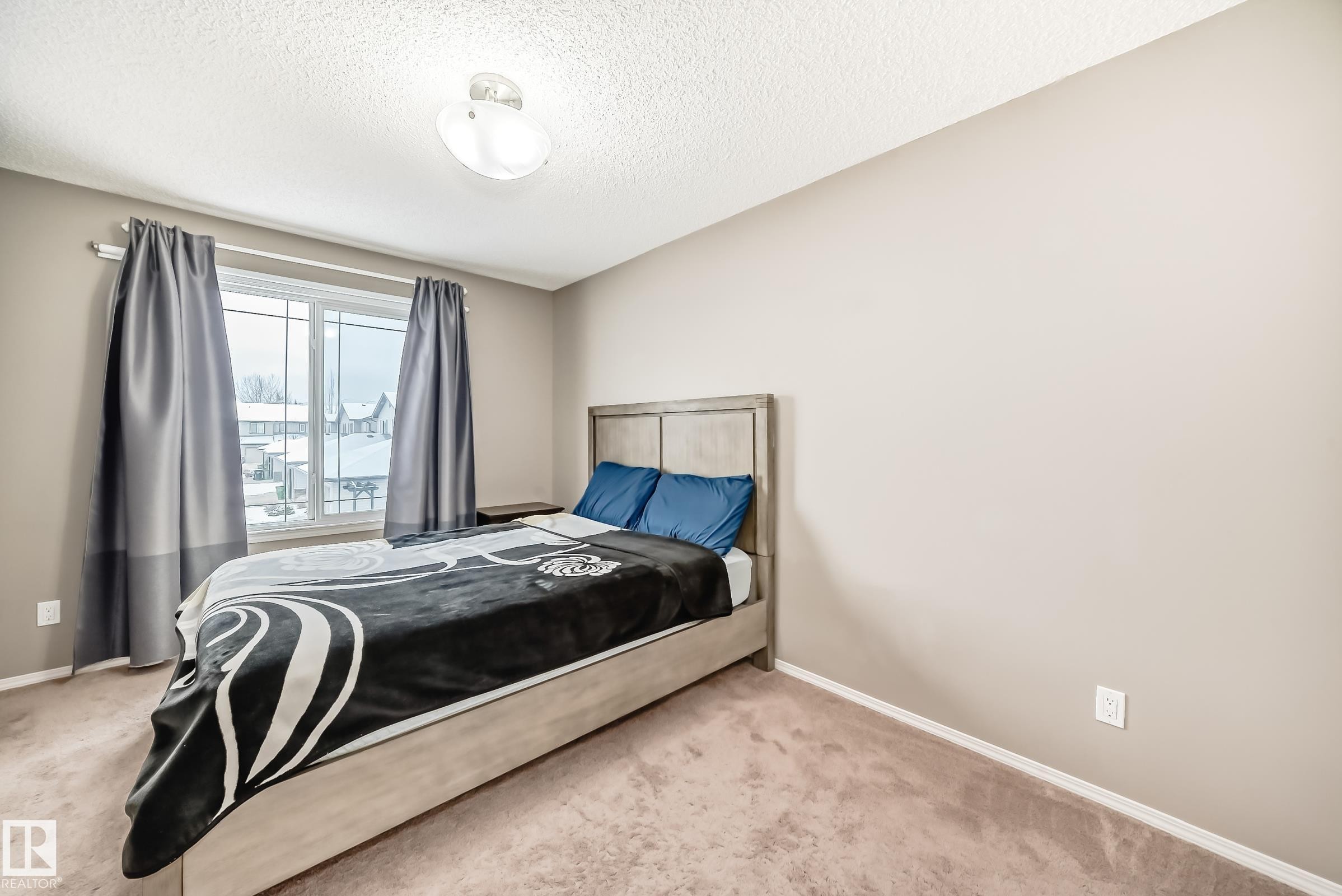This room features neutral-toned walls, a window with grey curtains, and carpeted flooring - 8 13838 166Ave, Edmonton, AB - Indoor Photo Showing Bedroom