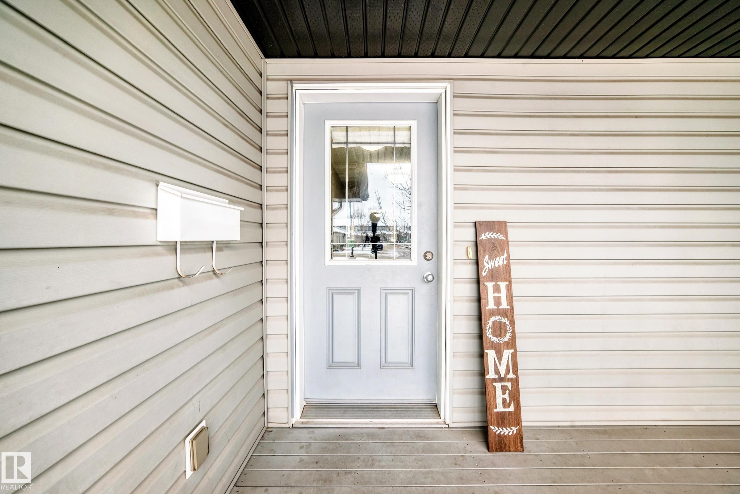 Inviting front porch entrance with light-colored siding and a grey front door featuring a glass insert - 8 13838 166Ave, Edmonton, AB - Outdoor With Exterior