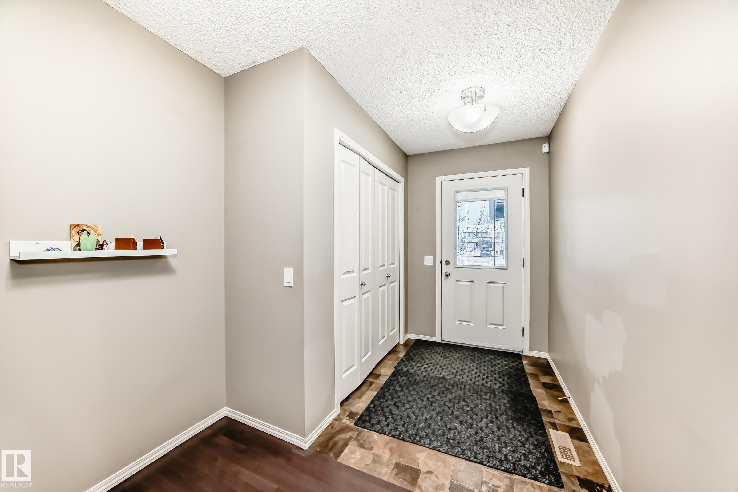 The entryway features a front door with decorative glass inserts, a ceiling-mounted light fixture, and a closet with bi-fold doors - 8 13838 166Ave, Edmonton, AB - Indoor Photo Showing Other Room