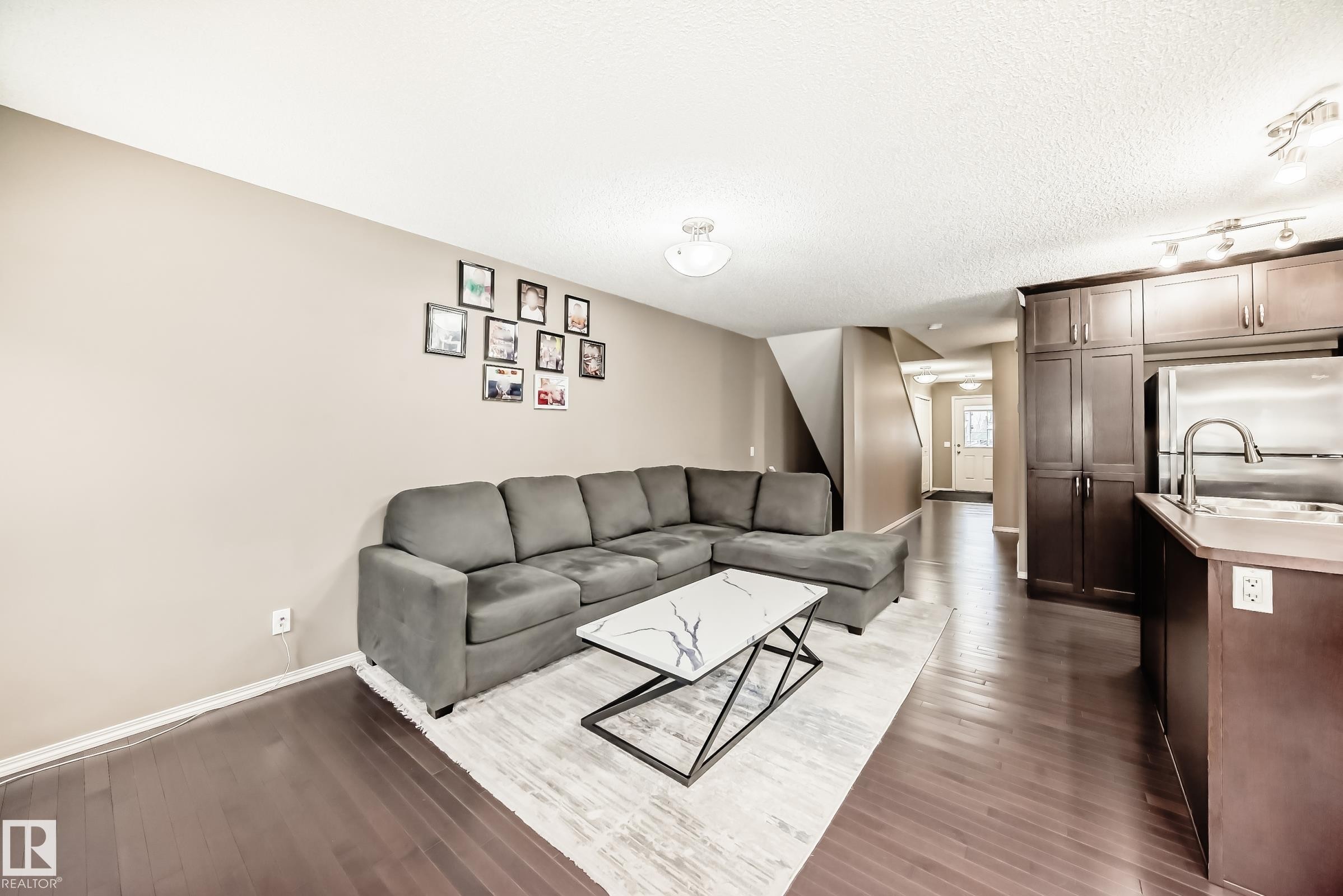 Living area featuring dark wood flooring, light-colored walls, and a view of the kitchen area - 8 13838 166Ave, Edmonton, AB - Indoor