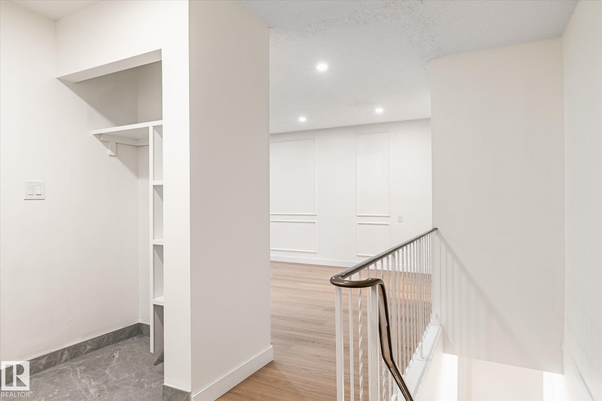 The property features a minimalist interior design with a built-in shelving unit, hardwood flooring, and recessed lighting - 6540 184 Street, Edmonton, AB - Indoor