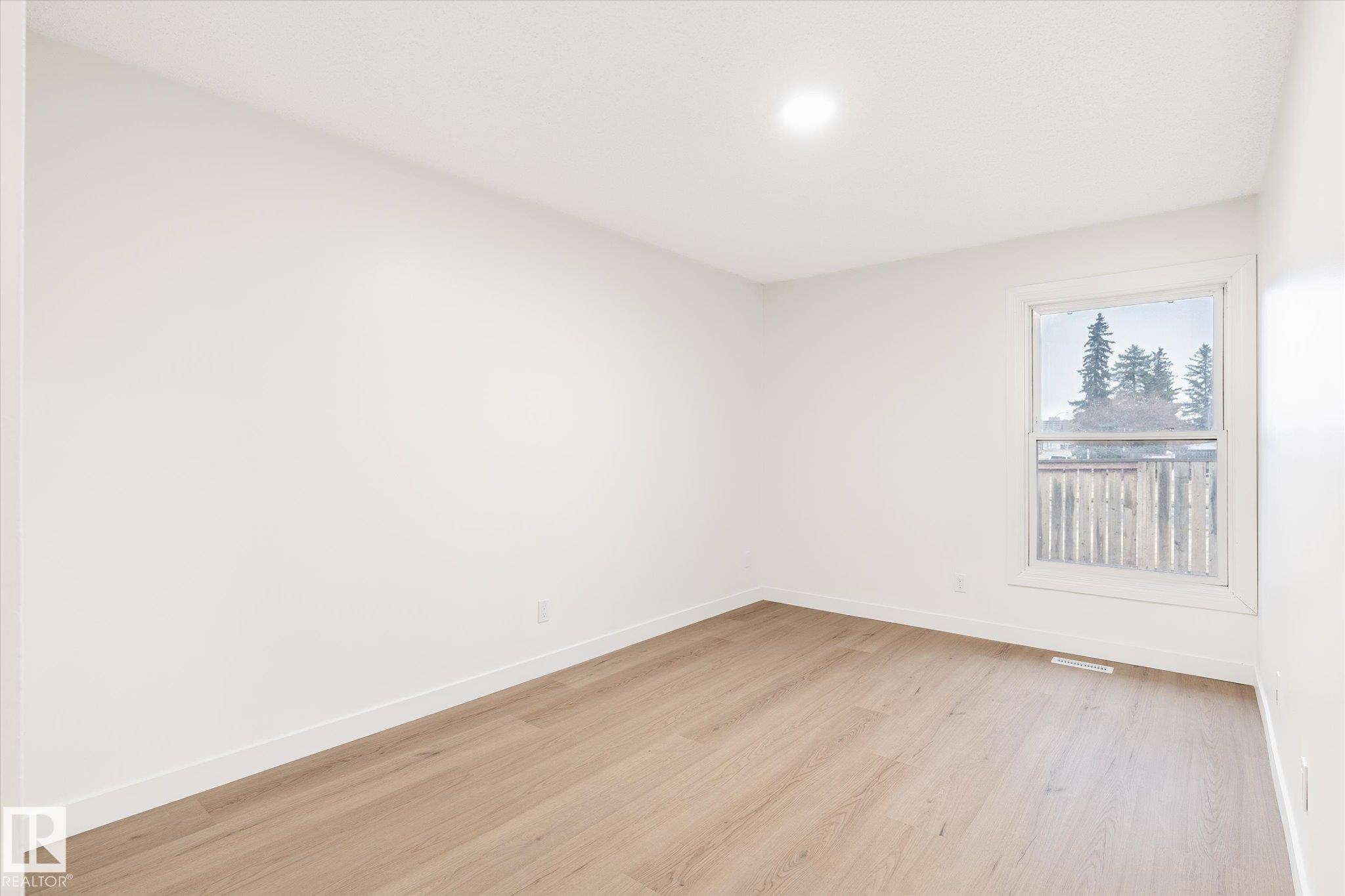 This room features light-colored walls, light wood flooring, and a window with a view of trees and a wooden fence - 6540 184 Street, Edmonton, AB - Indoor Photo Showing Other Room