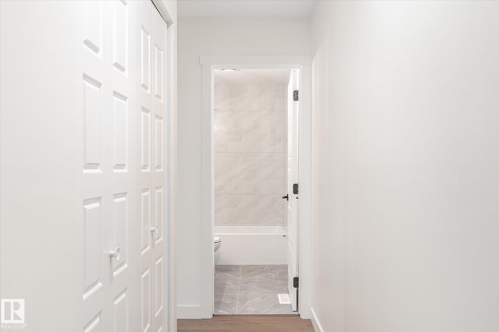 The property features white paneled doors and a hallway with light-colored walls, leading to a bathroom with a white bathtub and tiled walls - 6540 184 Street, Edmonton, AB - Indoor Photo Showing Other Room