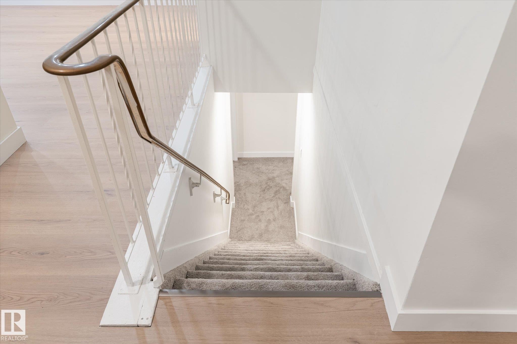 Staircase featuring a light-colored wood floor at the top, a carpeted runner on the stairs, and a metal handrail - 6540 184 Street, Edmonton, AB - Indoor Photo Showing Other Room