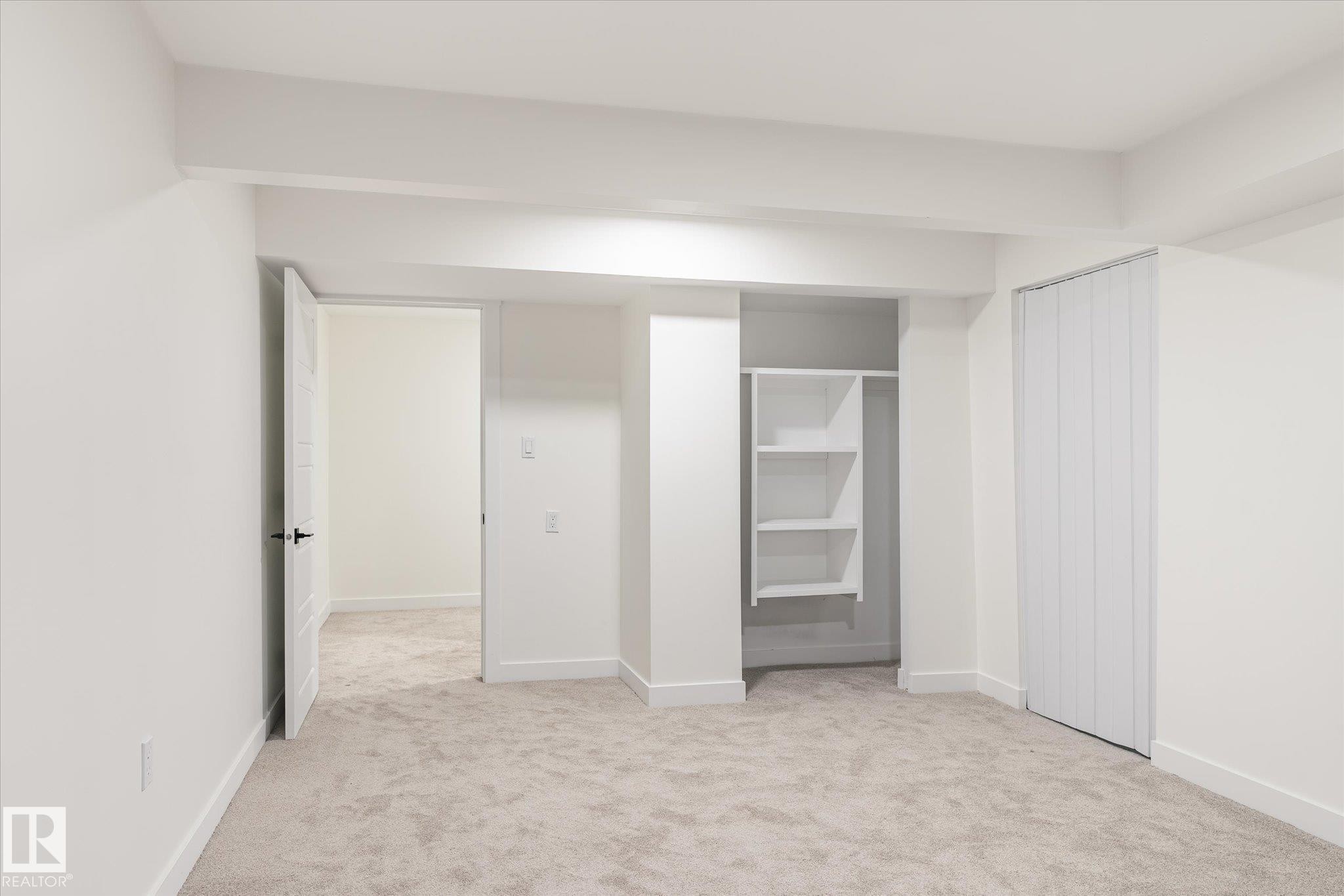 Carpeted room with white walls, an open doorway, an open closet with shelving, and a closed closet with vertical panel doors - 6540 184 Street, Edmonton, AB - Indoor Photo Showing Other Room