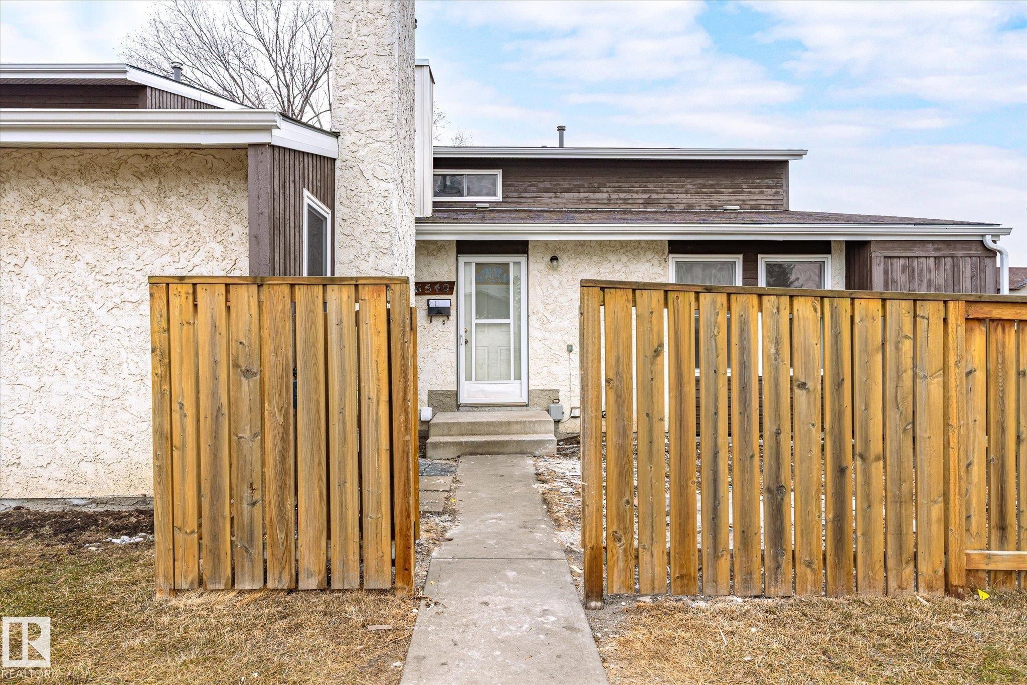 The property features a white front door and a concrete pathway leading to the entrance, framed by wooden fencing - 6540 184 Street, Edmonton, AB - Outdoor